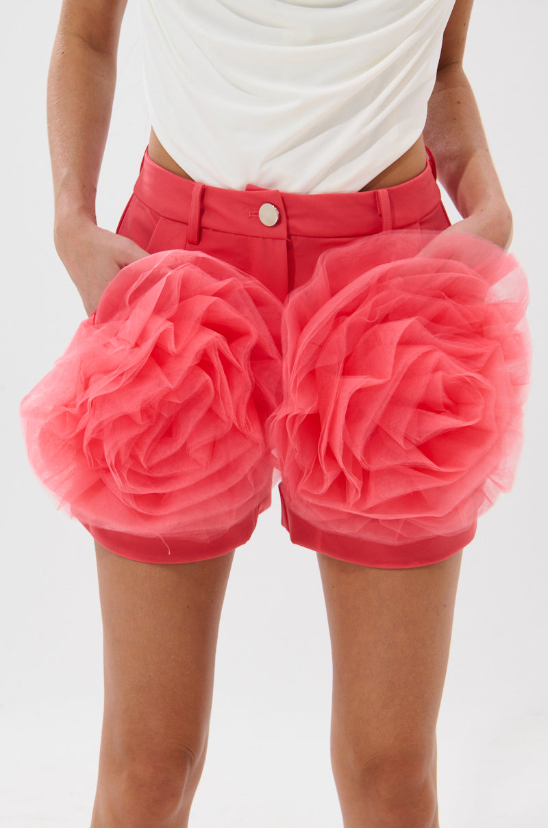 Wearing the IRIS FLORAL SHORT, featuring vibrant floral prints and bold 3D tulle appliqué on the pockets, paired with a white sleeveless top. The image is cropped at the waist and above the knees, highlighting playful festival style. 6