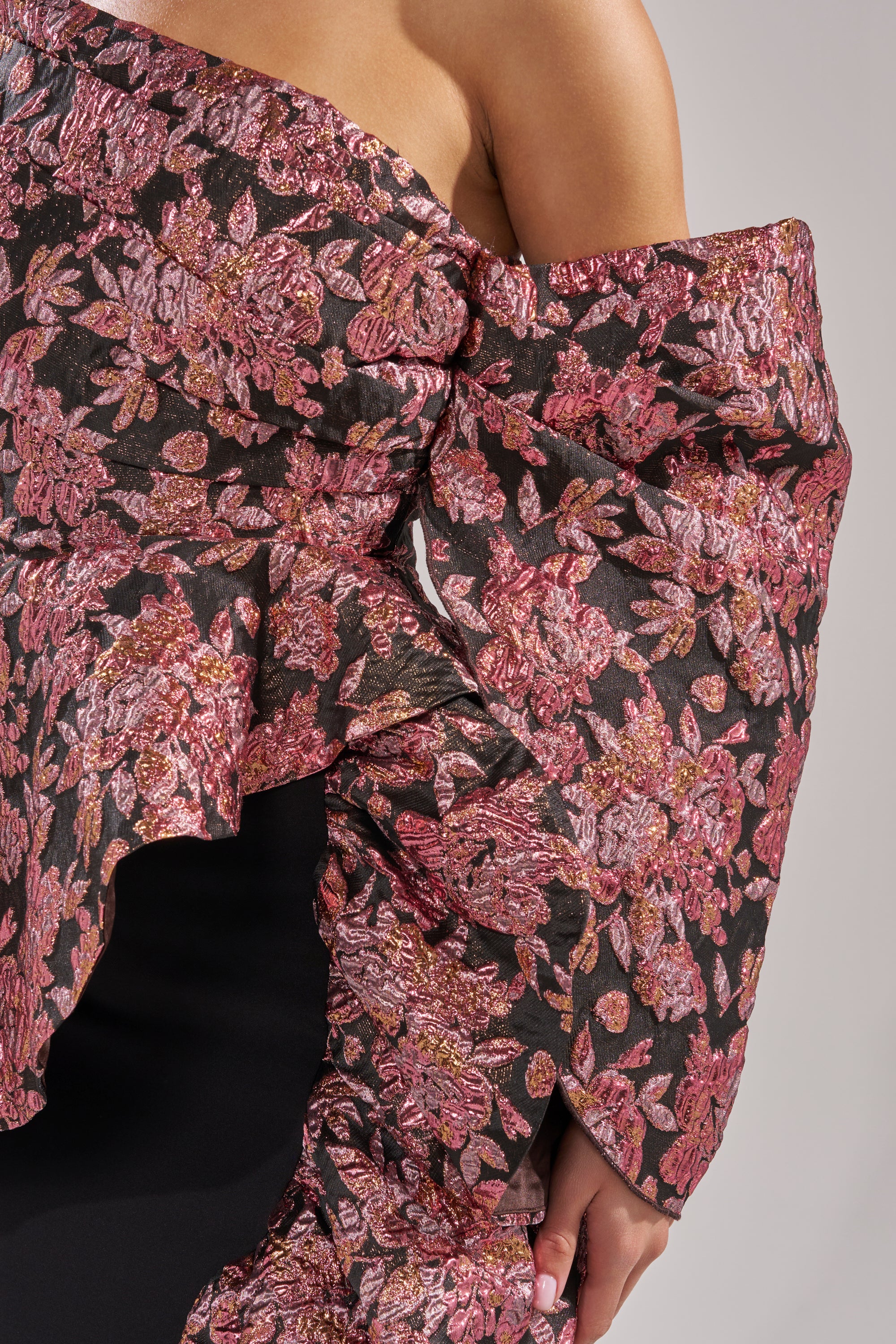 A close-up of a person wearing an off-the-shoulder top with a textured pink and gold floral pattern, paired perfectly with the SO MUCH IN LOVE BROCADE MAXI SKIRT—an ideal choice for any holiday party ensemble.