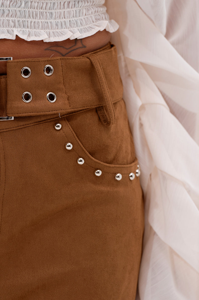 Close-up of a person wearing the FIGURE IT OUT FAUX SUEDE SHORT, featuring silver studs along the pocket edge, paired with a textured white top and flowing white garment. A small tattoo is visible near the waistband. 6