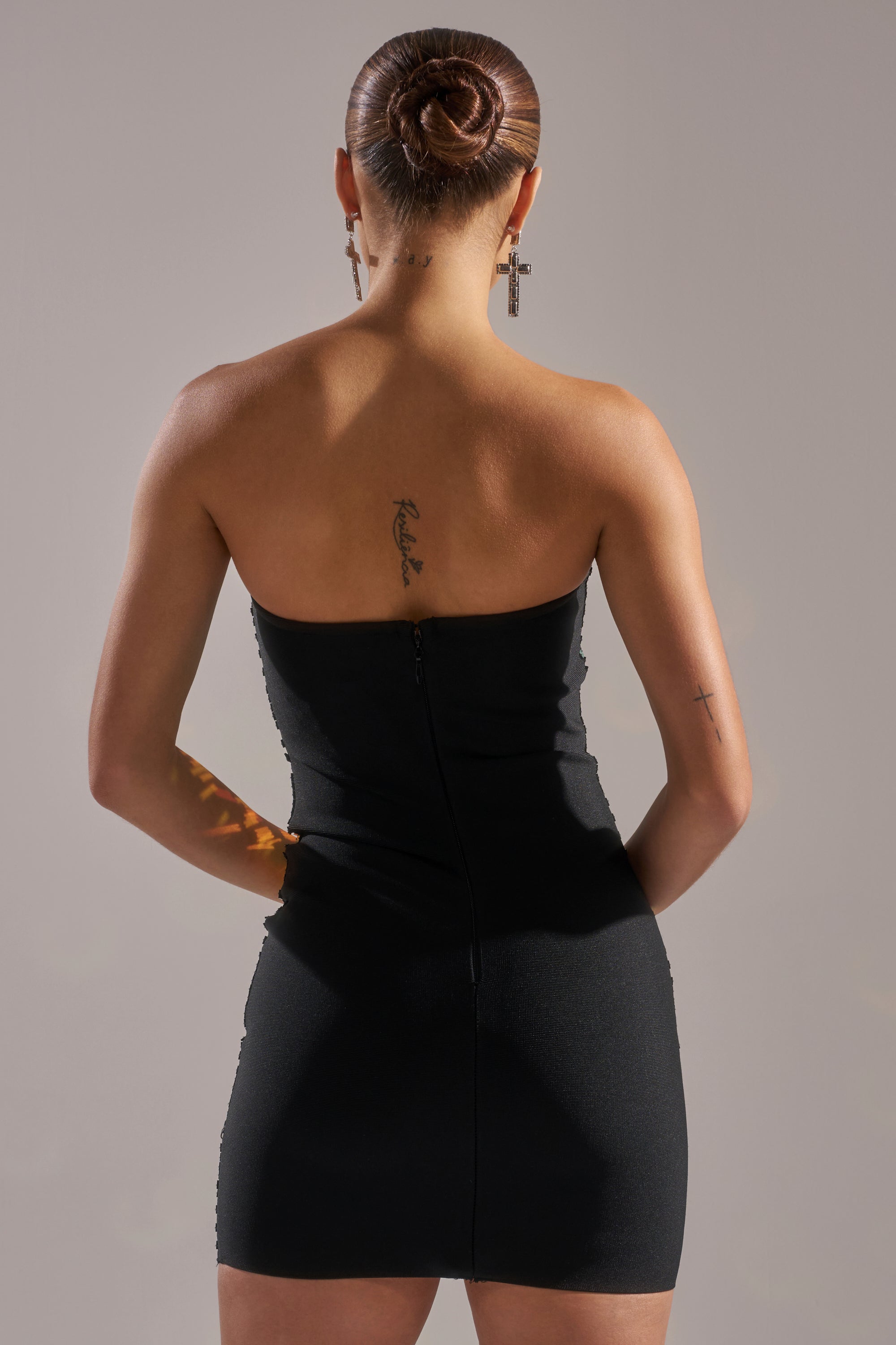 A person with their hair in a bun, shown from the back, wears the DANCIN THE NIGHT AWAY MINI DRESS. Tattoos on their upper back and arm are visible as they stand against a neutral background.