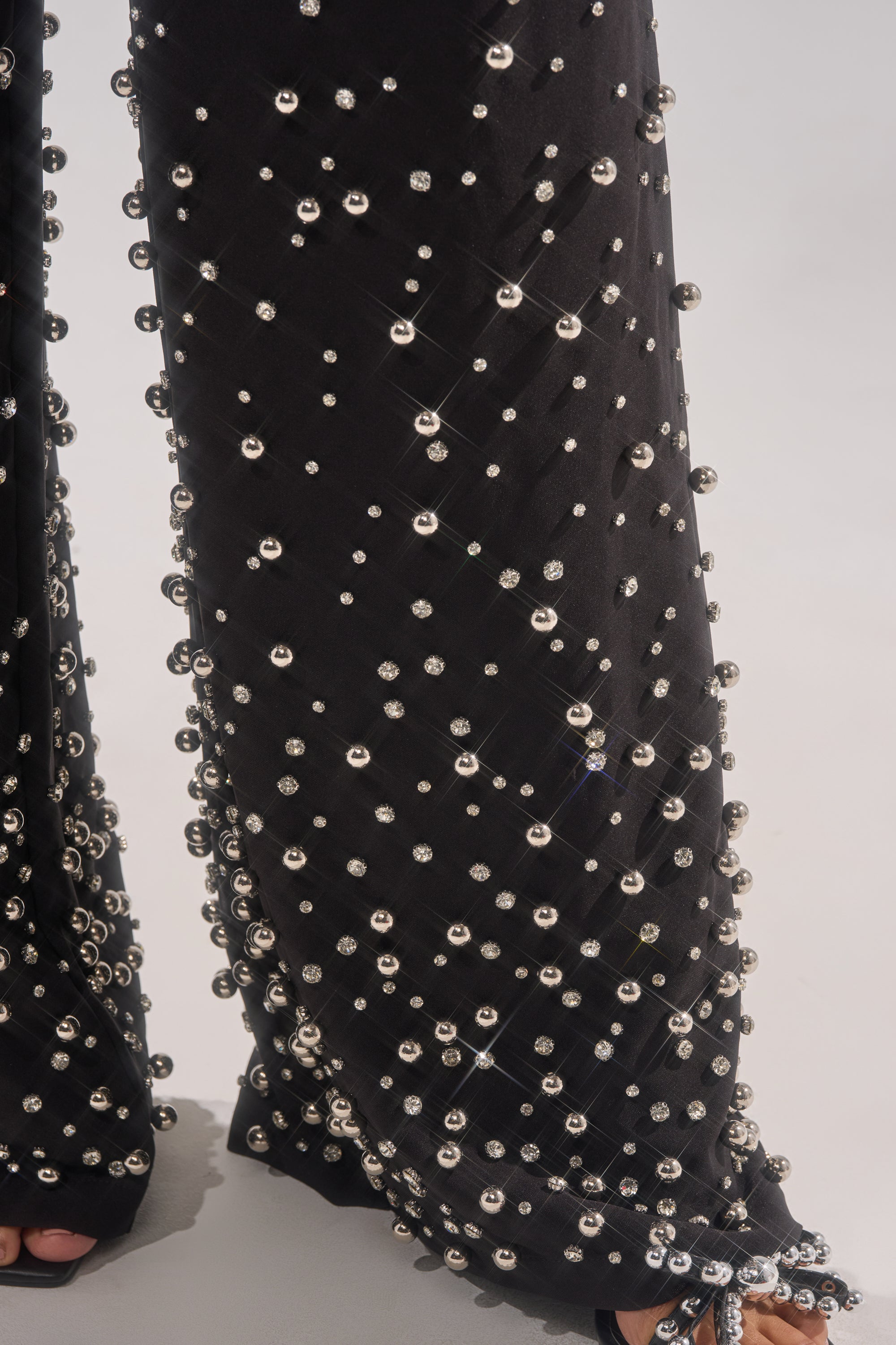Close-up of the GET CLOSER EMBELLISHED TROUSER, showcasing a grid of silver beads, rhinestone detailing, a slightly flared wide-leg hem, and a peek of a sandal at the bottom.