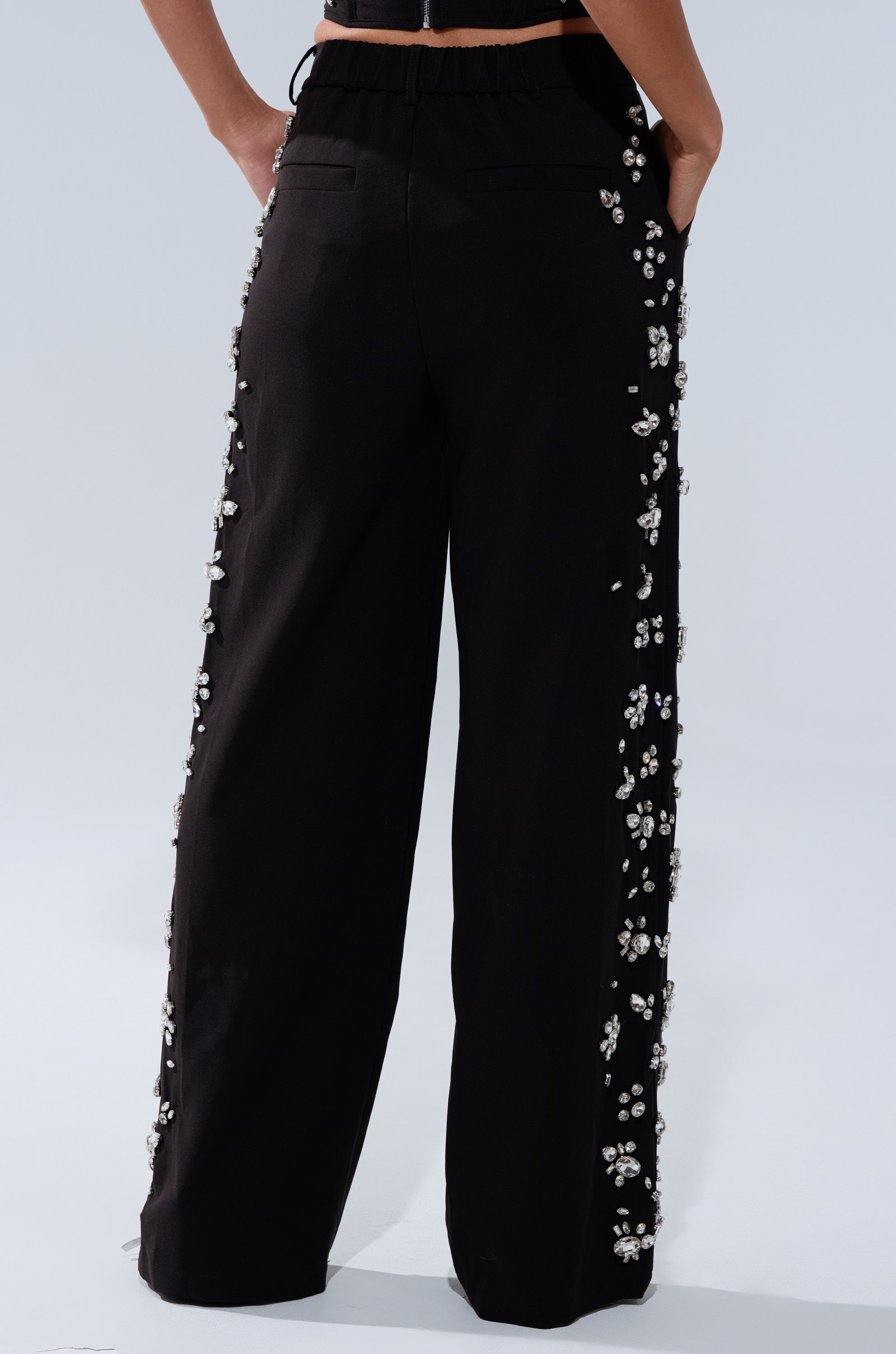 A person wears high-waisted wide-leg pants with hands in pockets; rhinestones embellish the outer seams, capturing the luxe vibe of the FEELING RICH TROUSER WITH RHINESTONE.