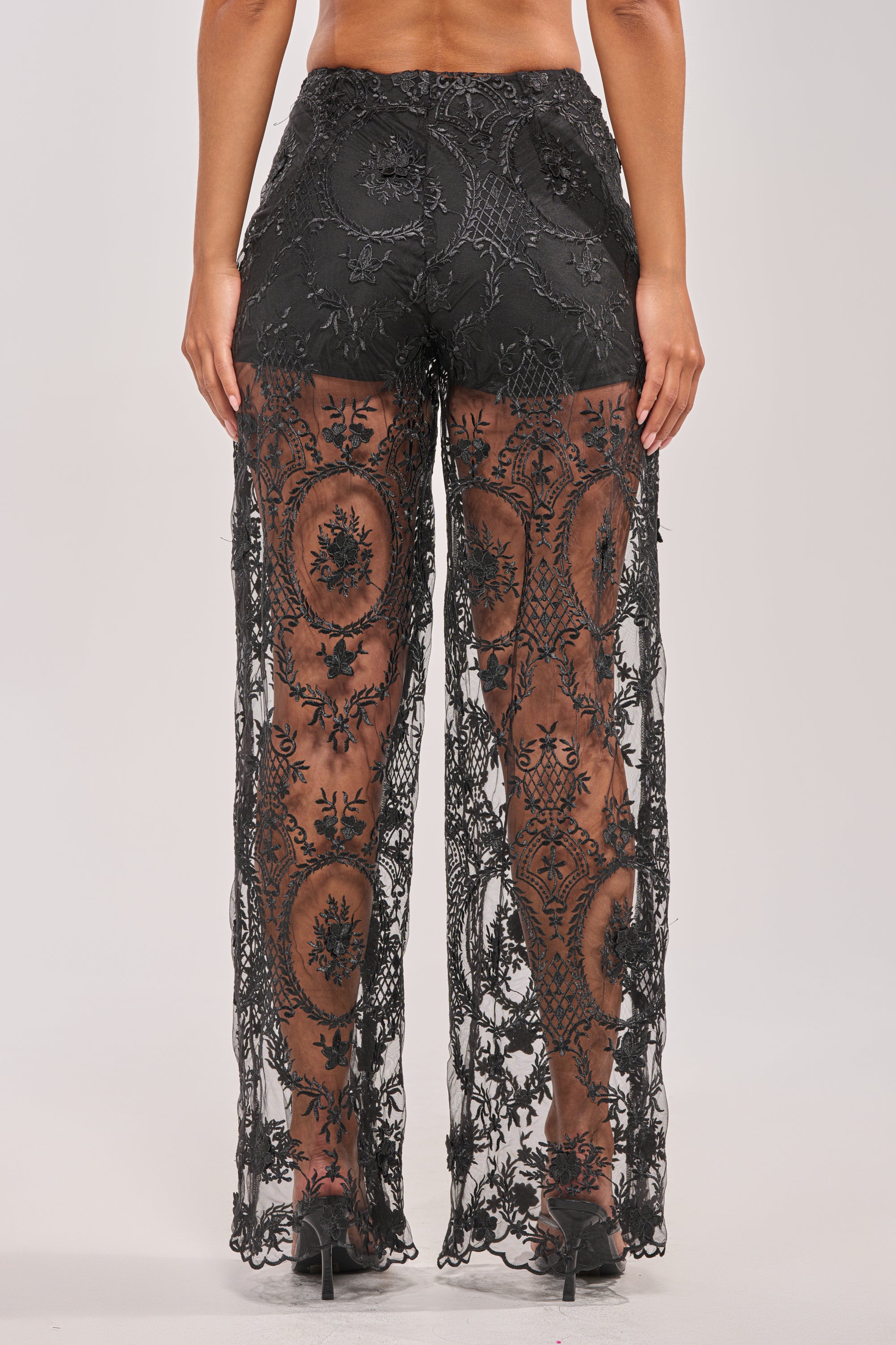 A person faces away, wearing SUPER LUXE WIDE-LEG PANT—black sheer lace over black shorts with floral embroidery—paired with black high heels. 4