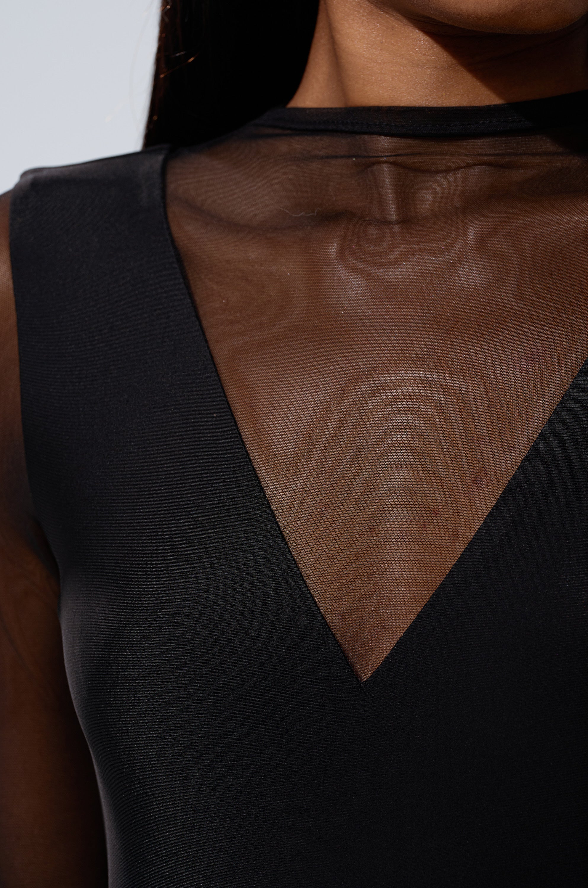 Close-up of a person wearing the EASY LOVING MESH JUMPSUIT, featuring black sheer fabric with a mesh V-shaped neckline that reveals part of the upper chest and shoulder for an elegant, modern look.