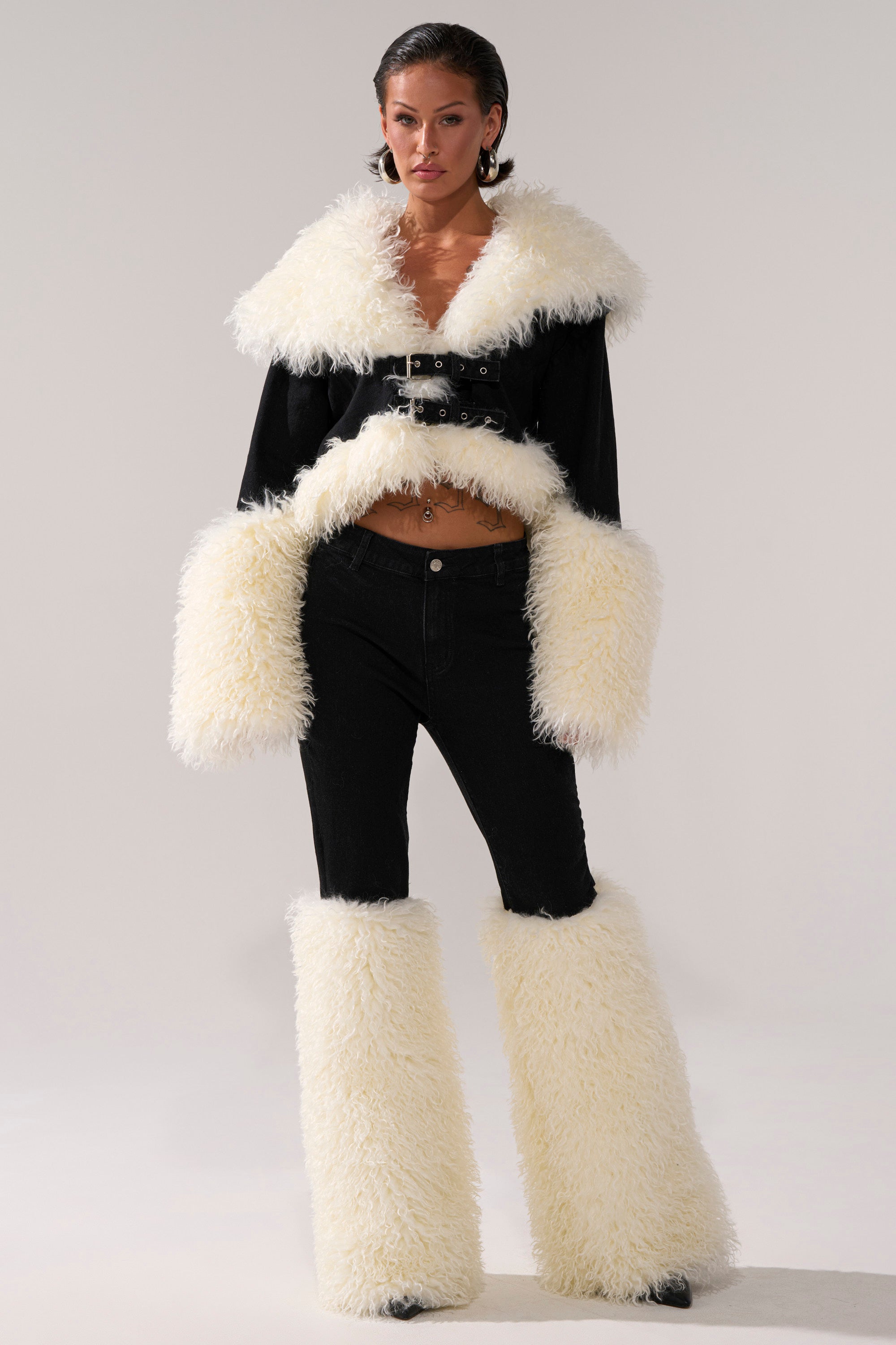 A person stands facing forward in the SITTING PRETTY FUR TRIM DENIM outfit, featuring dramatic, fluffy white fur trim on the collar, sleeves, and lower legs. The background is plain and light-colored.