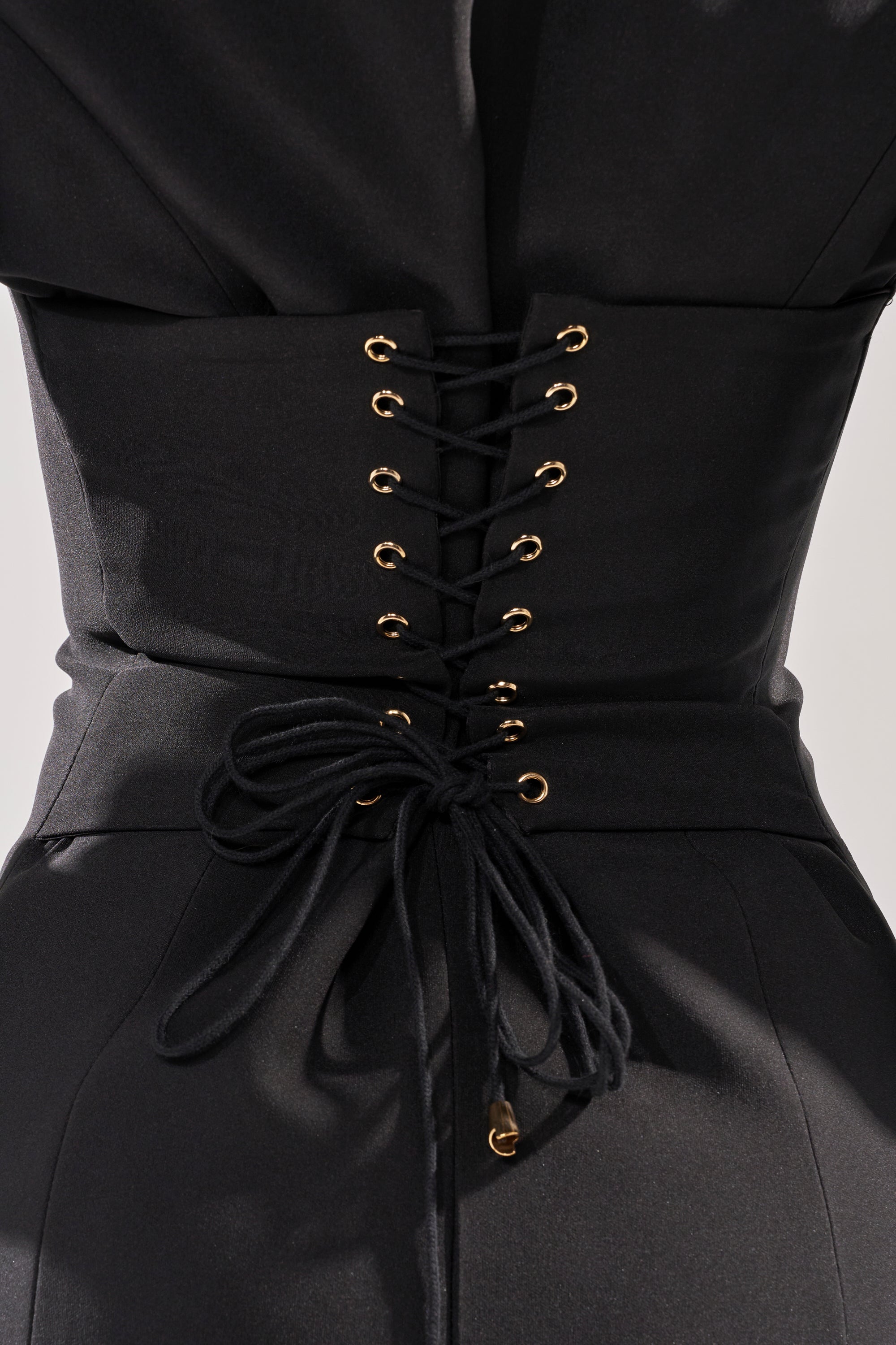 Close-up of the OK BOSS LADY BLAZER MAXI DRESS, highlighting black fabric with gold eyelets and black laces in a bow on the lace-up back panel, styled over matching black pants. 8