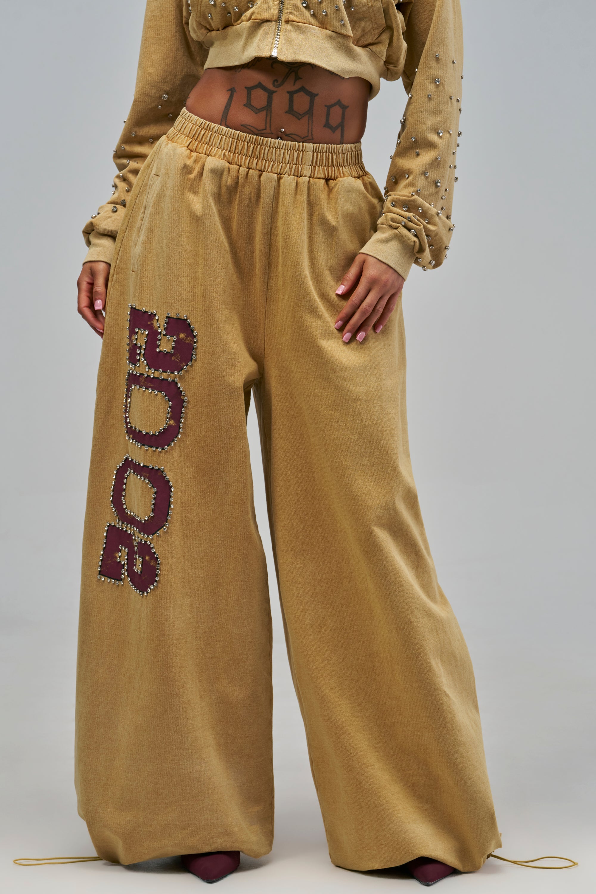 Mustard WINNERS CLUB WIDE LEG JOGGER with an elastic waistband and vertical maroon lettering accented by metallic studs.