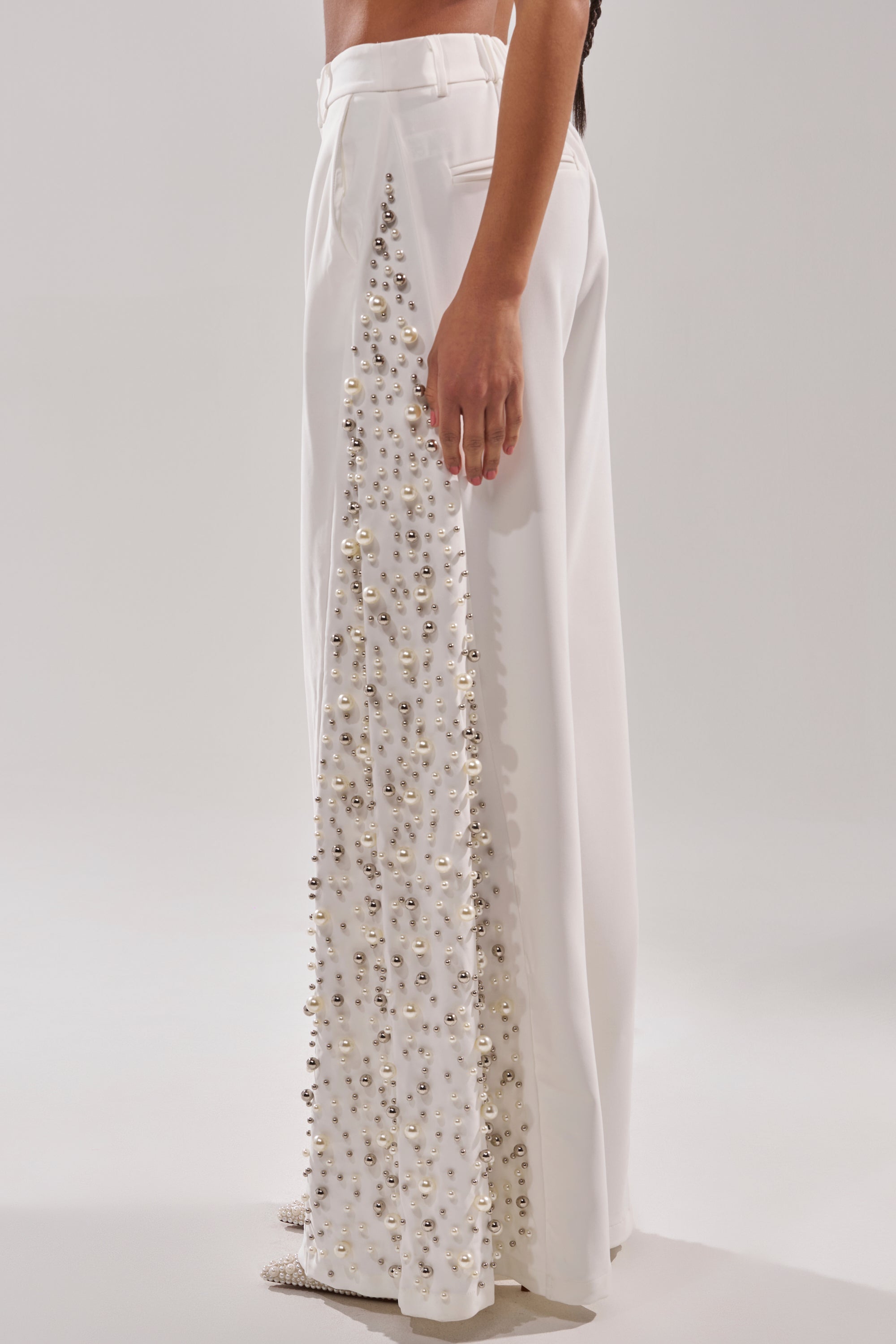 A person wears the KEEP IT GOING EMBELLISHED TROUSER, featuring pearl beading and a beautifully embellished side panel, standing against a plain light background.