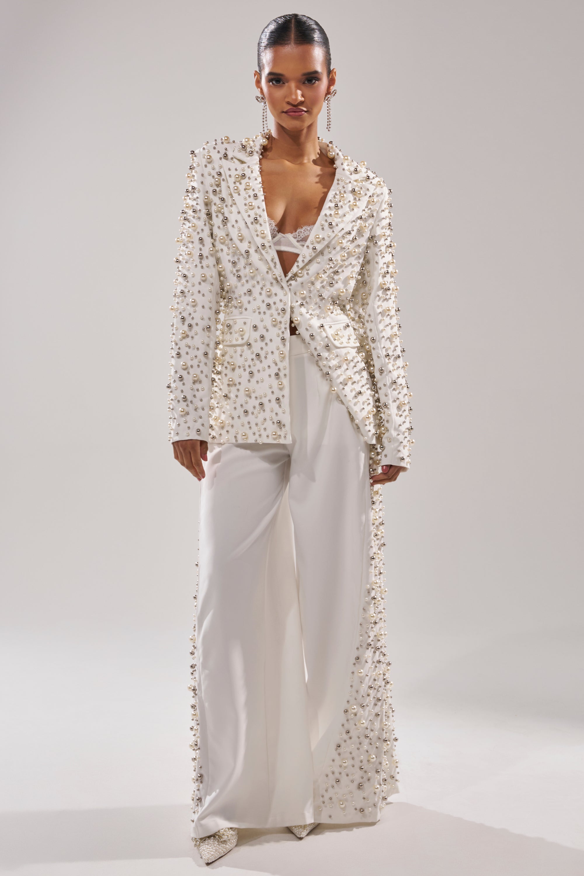 A model wears the KEEP IT GOING EMBELLISHED BLAZER—white with intricate bead and sequin details—over matching wide-leg pants and a bralette, standing against a plain light background.