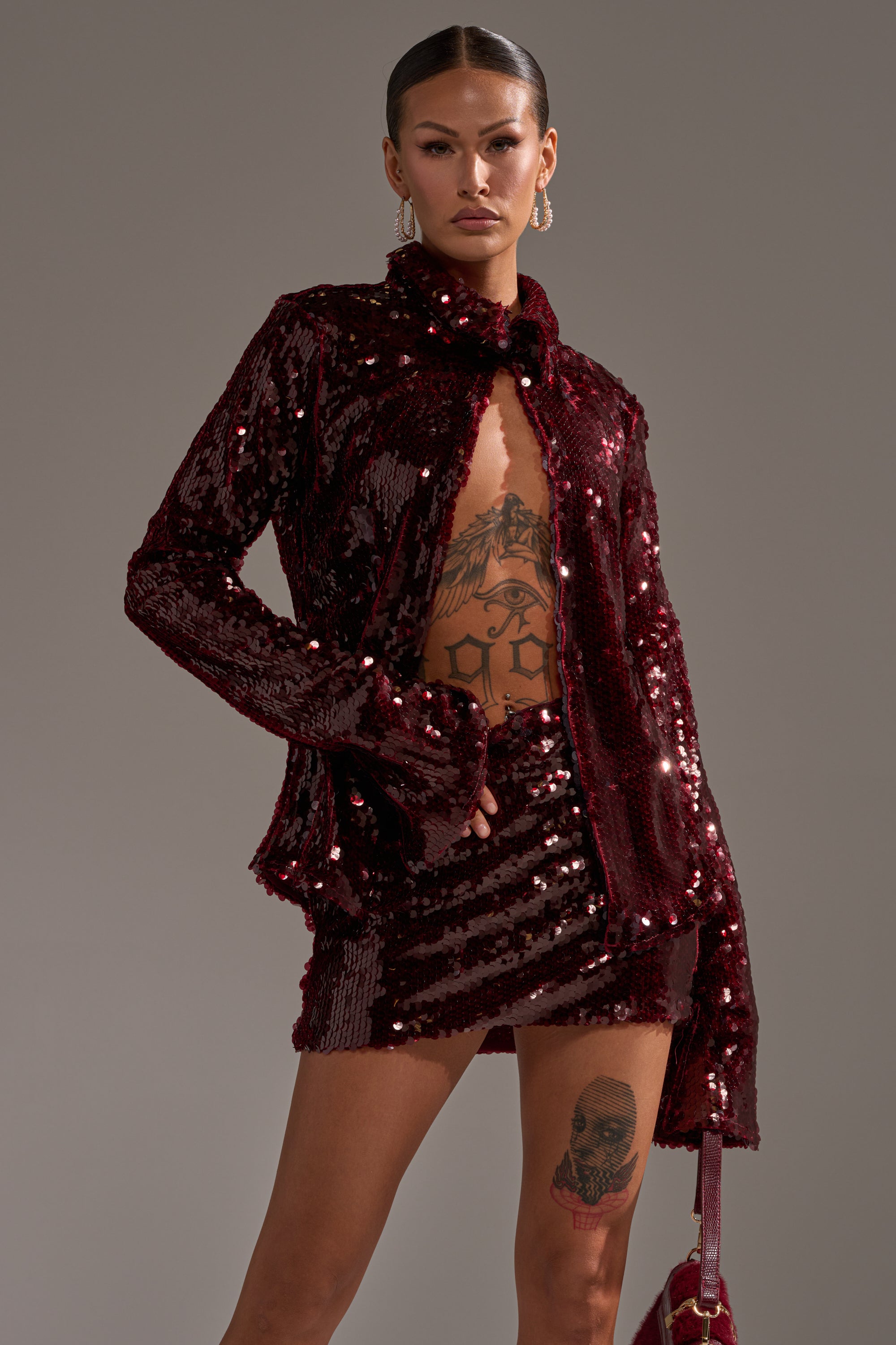 A person wearing the SHINING DOWN ON YOU SEQUIN BUTTON DOWN and matching mini skirt stands confidently, showing off tattoos and a small bag—hair pulled back, making this look perfect for a standout holiday party ensemble.