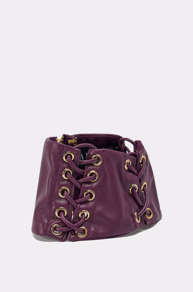 The WHAT THE HELLY CHOKER is a faux leather accessory, perfectly paired with a purple AKIRA Label belt featuring gold eyelets and crisscrossed lace for a bold, corset-inspired look against a light background. 2