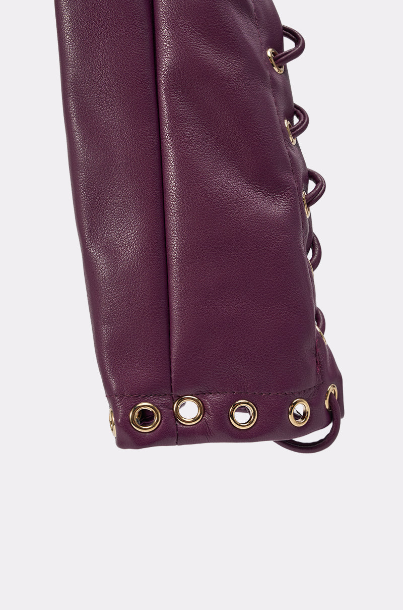 Close-up of WHAT THE HELLY GLOVES, purple leather with gold eyelets and lace-up sides. The textured leather and shiny metal eyelets stand out, matching perfectly with lace-up accessories. 9