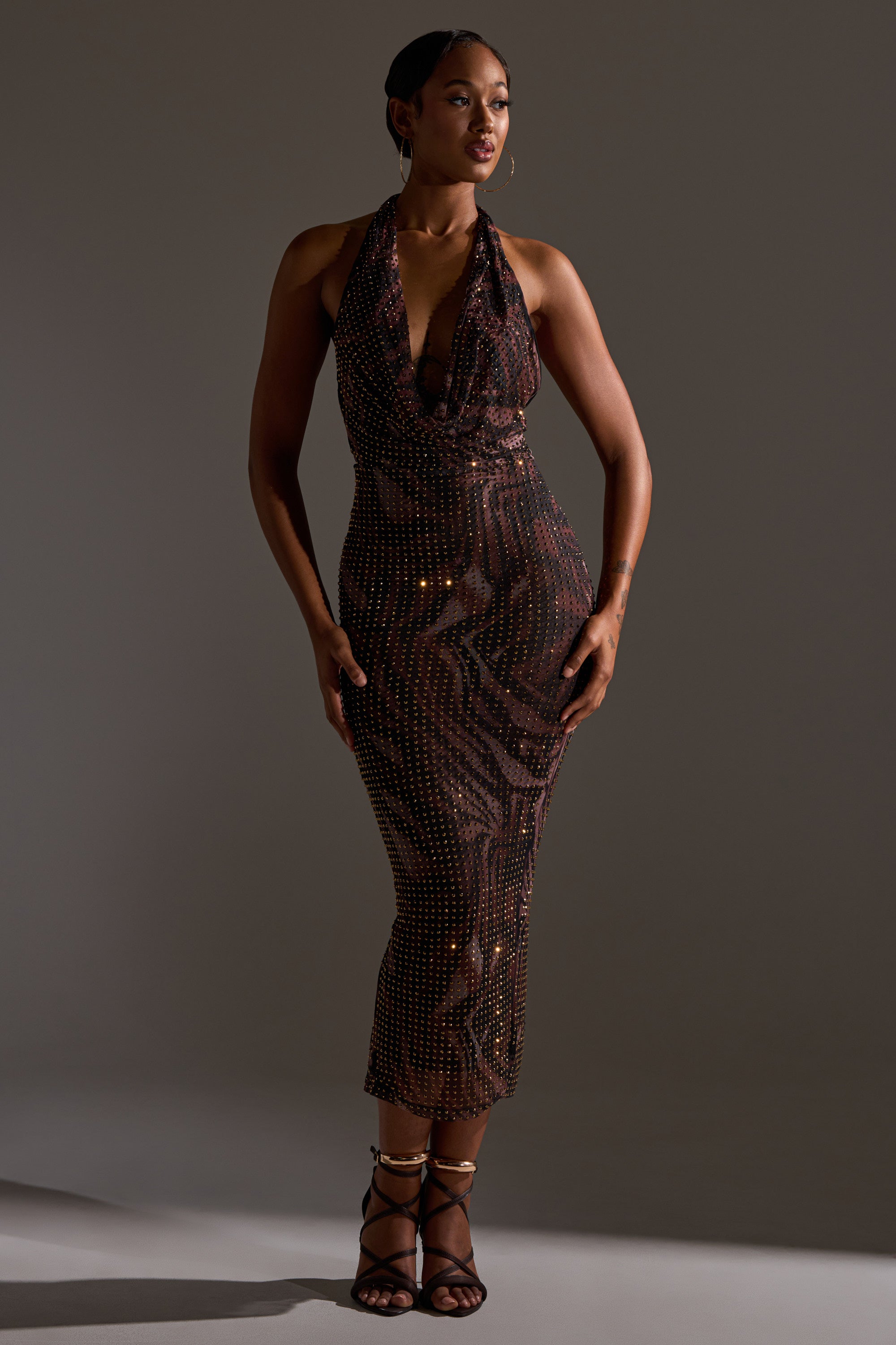 A woman poses in the LENNON PRINTED MESH RHINESTONE MIDI DRESS, featuring a bodycon fit and sparkling rhinestone details, styled with strappy black heels against a plain dark background.