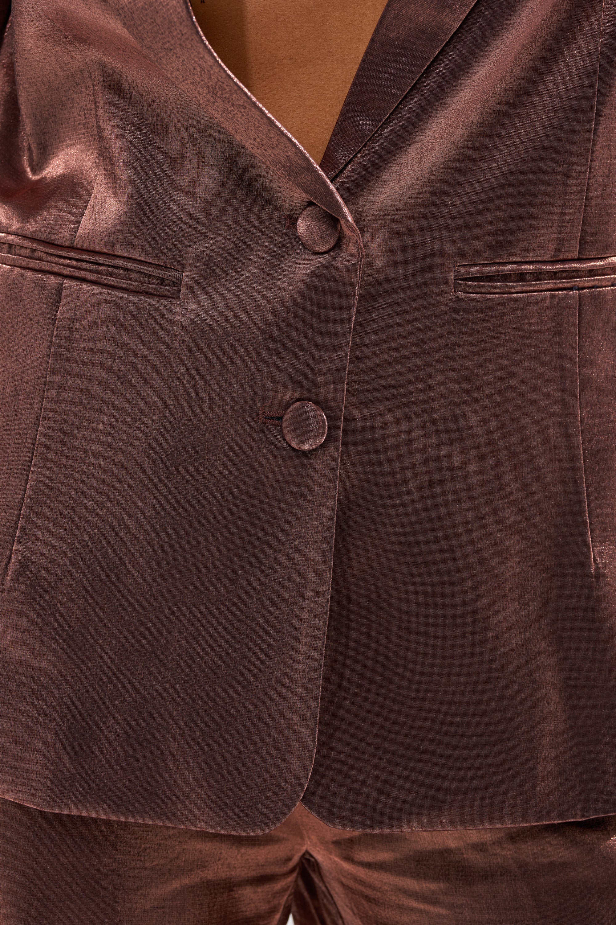 Close-up of the STAY CLOSE IRIDESCENT BLAZER in shiny dark mauve, featuring two buttons and narrow front pockets, worn over matching pants. The blazer’s smooth, satin-like fabric has an iridescent sheen. 1
