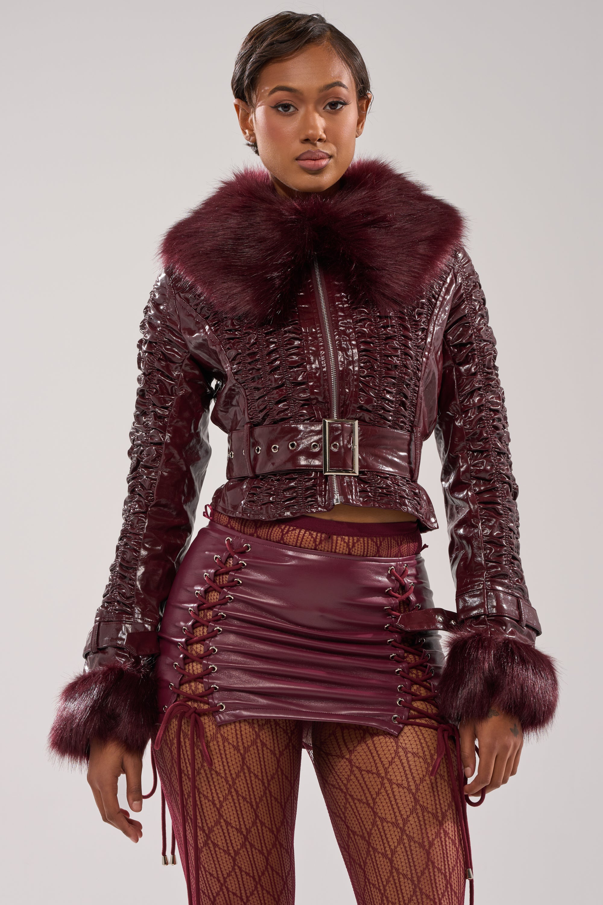 A woman models the IF YOU'RE DOWN FUR TRIM MOTO jacket with a large collar and cuffs, styled with a coordinating lace-up mini skirt and patterned tights against a plain background.