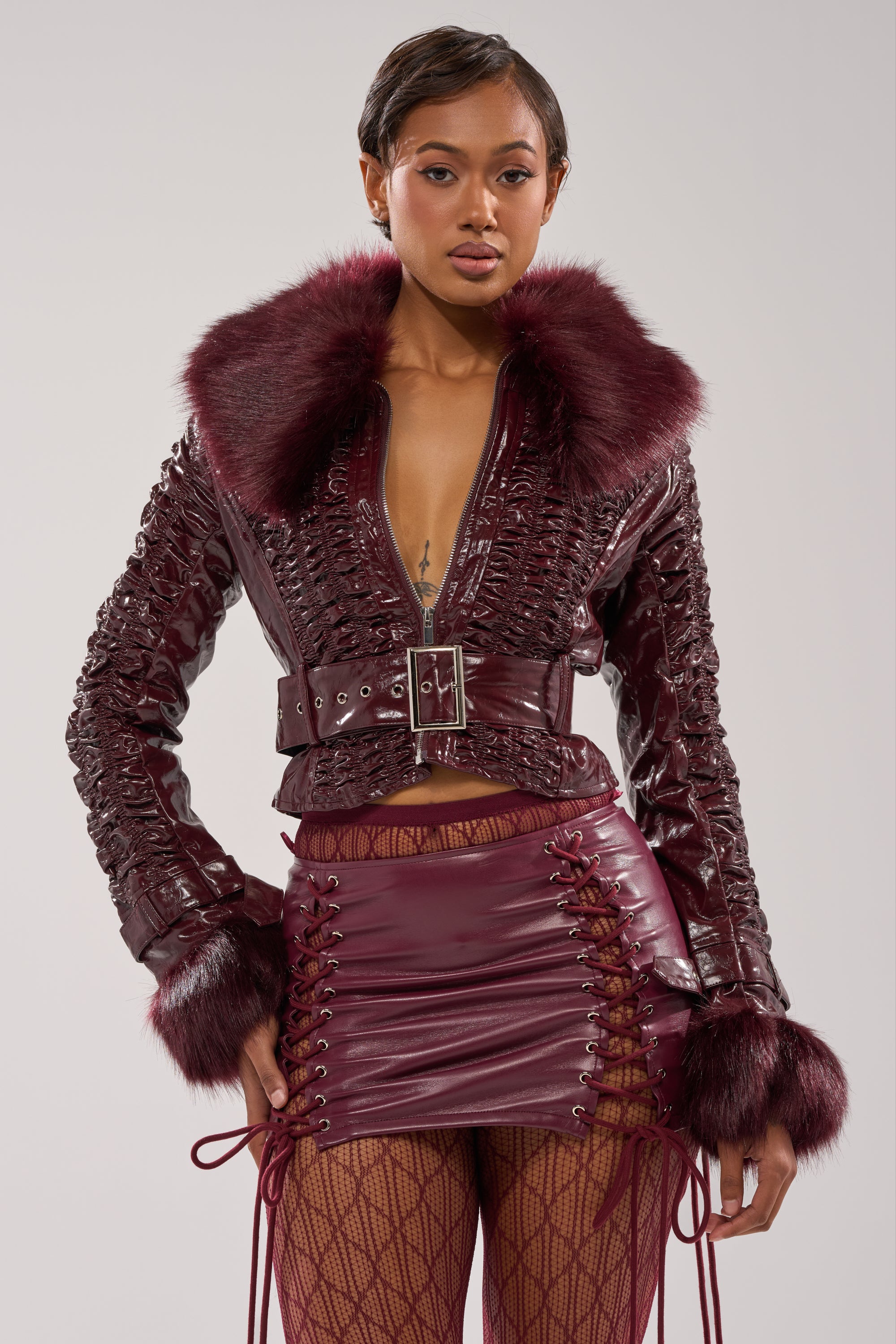 A woman in winter streetwear wears the IF YOU'RE DOWN FUR TRIM MOTO jacket with a lace-up mini skirt and patterned tights, styled against a plain light background.