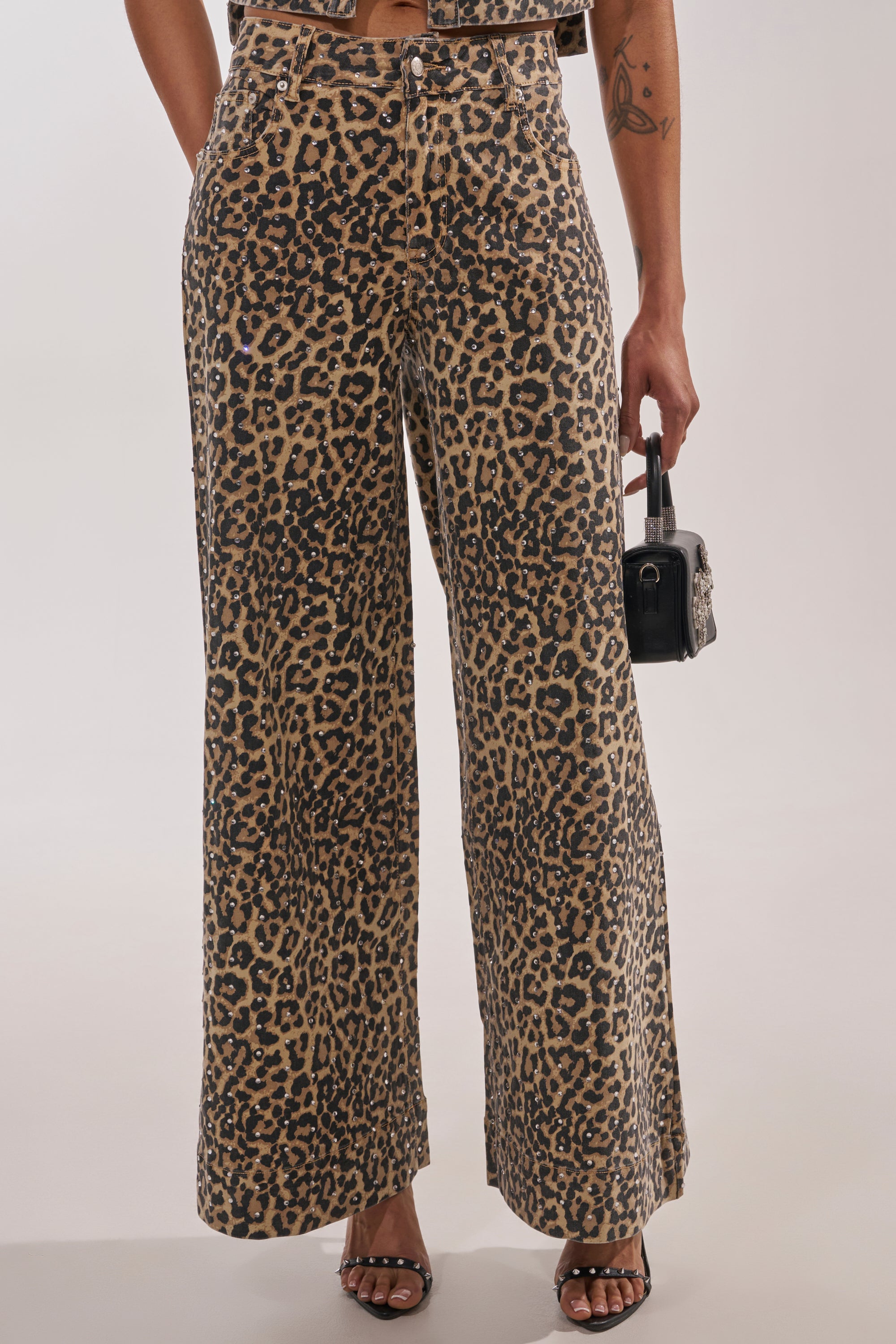 Wearing LEOPARD SISTA RELAXED DENIM, styled with open-toe sandals and a small black handbag; only the person's upper body is partially visible. 1