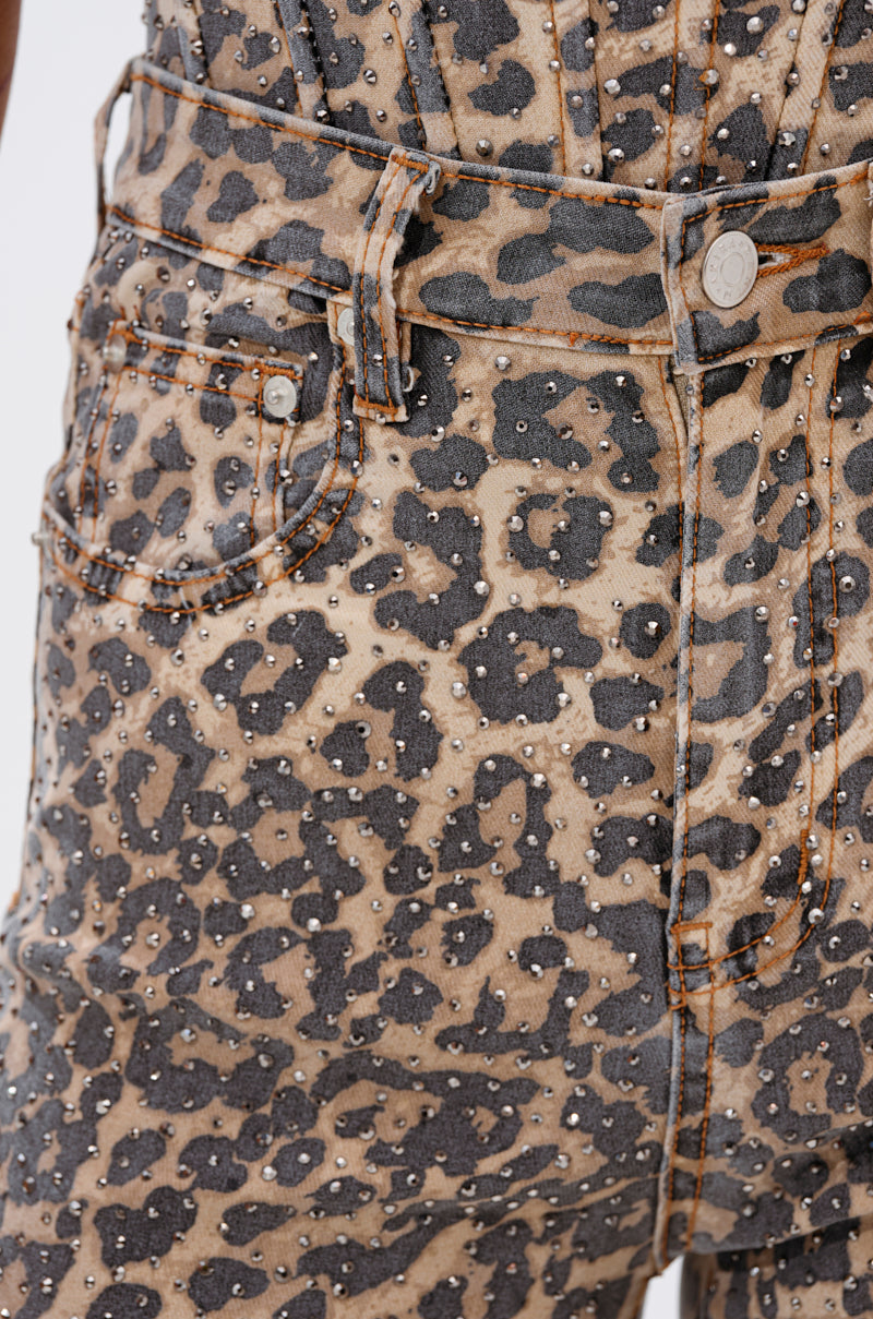 Close-up of a person's waist and hip wearing the IN THE WILD WIDE LEG CHEETAH PANT in stretchy denim, featuring a high-waisted, wide-leg fit with metallic studs, orange stitching, and a silver button at the waistband.