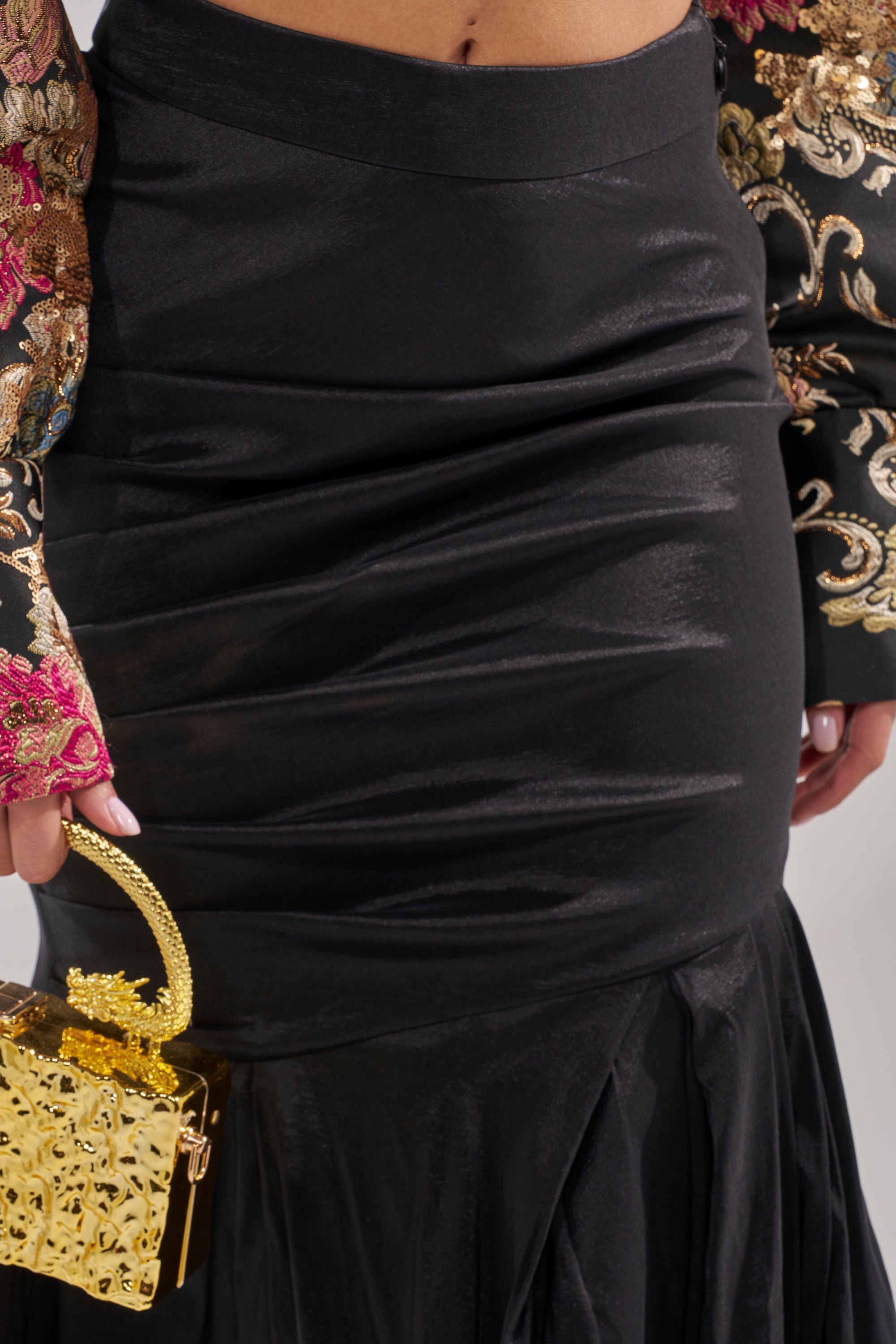 Wearing the QUEEN OF IT ALL MAXI SKIRT—a fitted black satin maxi with a subtle mermaid hem—paired with an ornate embroidered sleeve and a gold handbag makes for an elegant look at formal events.