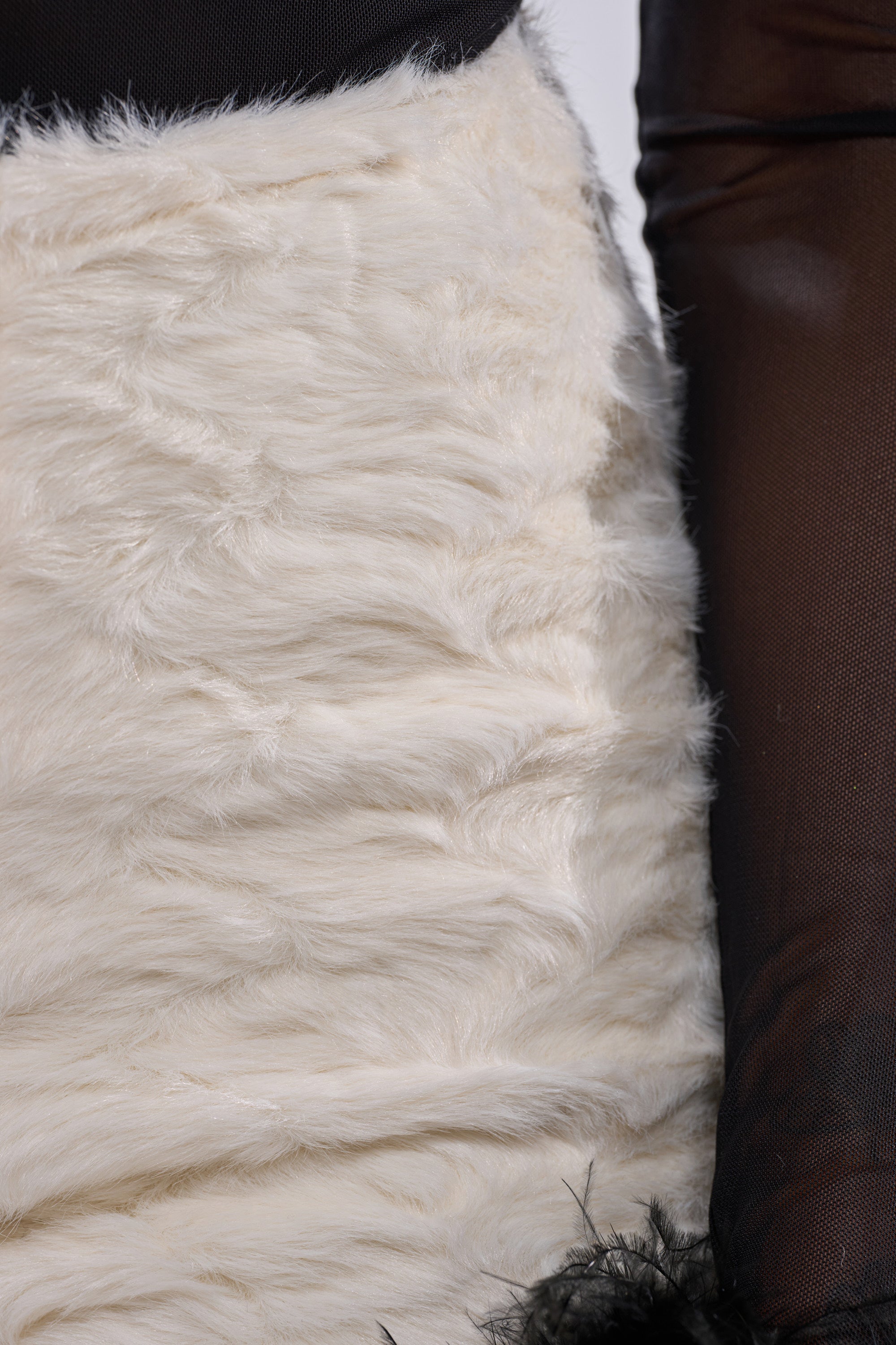 Close-up of someone wearing the TOUCH ME FUR SHORT in soft white faux fur, paired with a sheer black long-sleeve top. The mix of plush fur shorts and mesh sleeves showcases standout street-luxe style details. 9