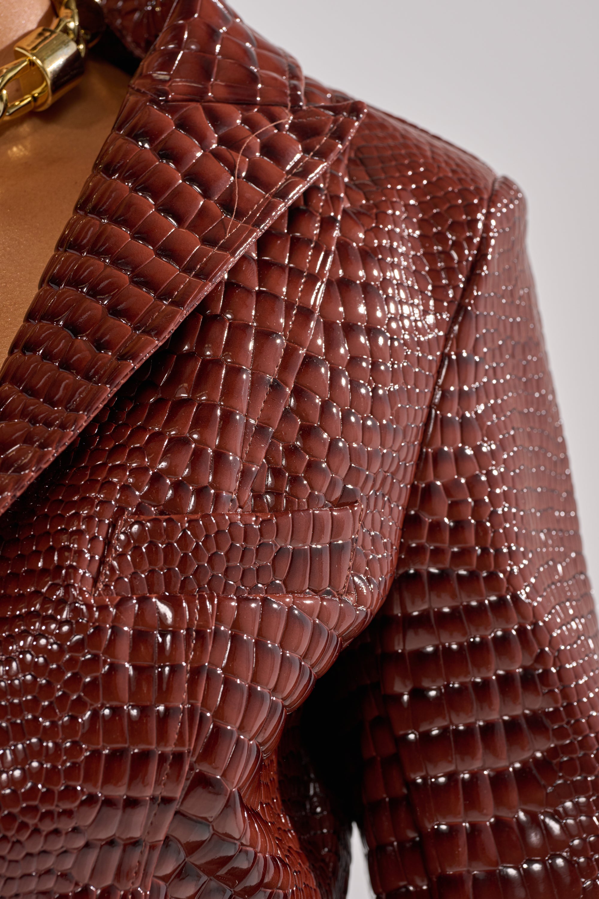 Close-up of the NEW FLAME EMBOSSED PATENT BLAZER, featuring a shiny dark brown crocodile-print texture, embossed patent finish, and notched lapel. 8