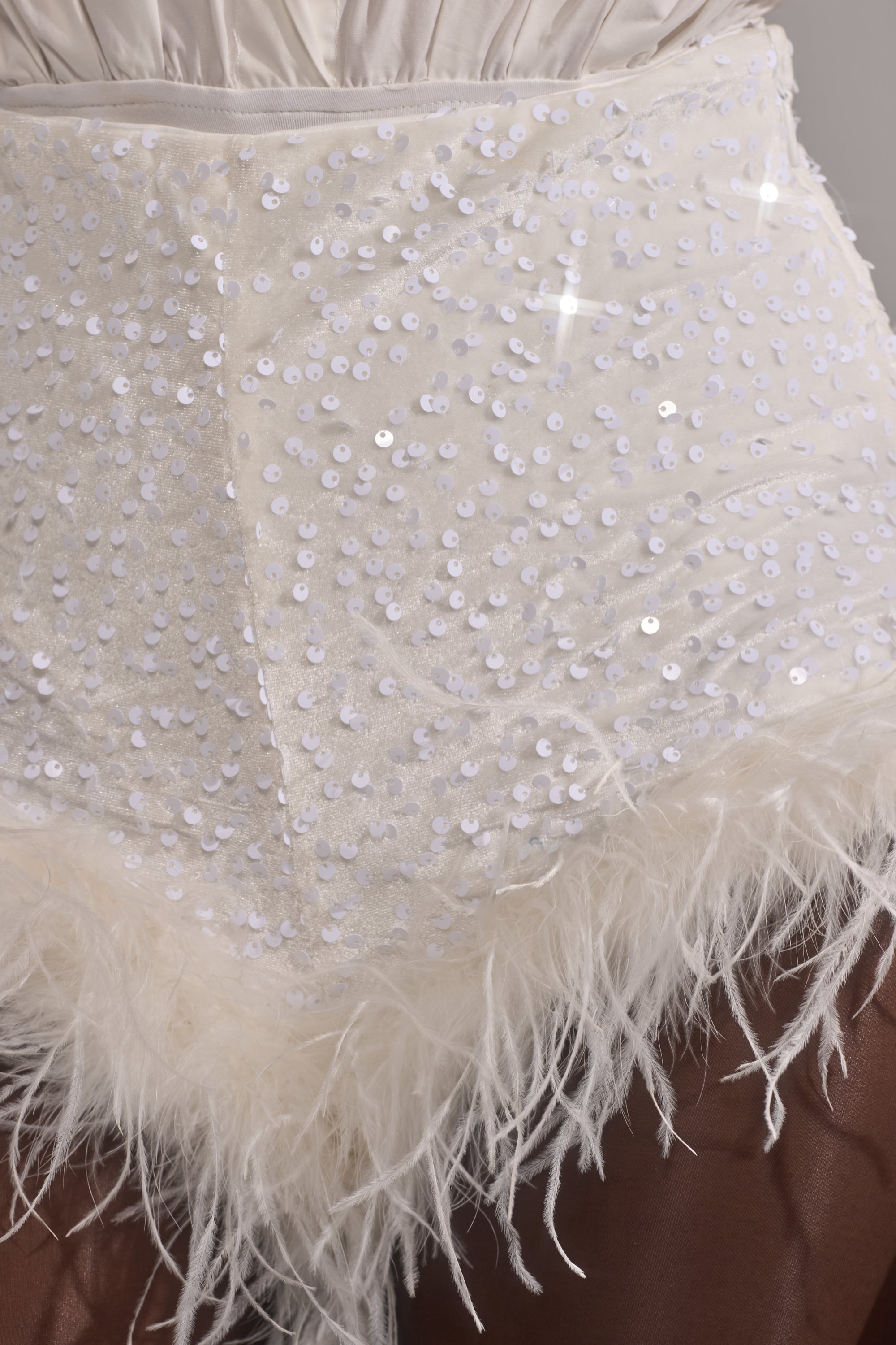 Close-up of NEW YEAR FEATHER SHORTS—high-rise mini shorts with white sequins that sparkle and a feather trim at the hem, adding soft, textured detail. Worn by a person with dark skin. 10