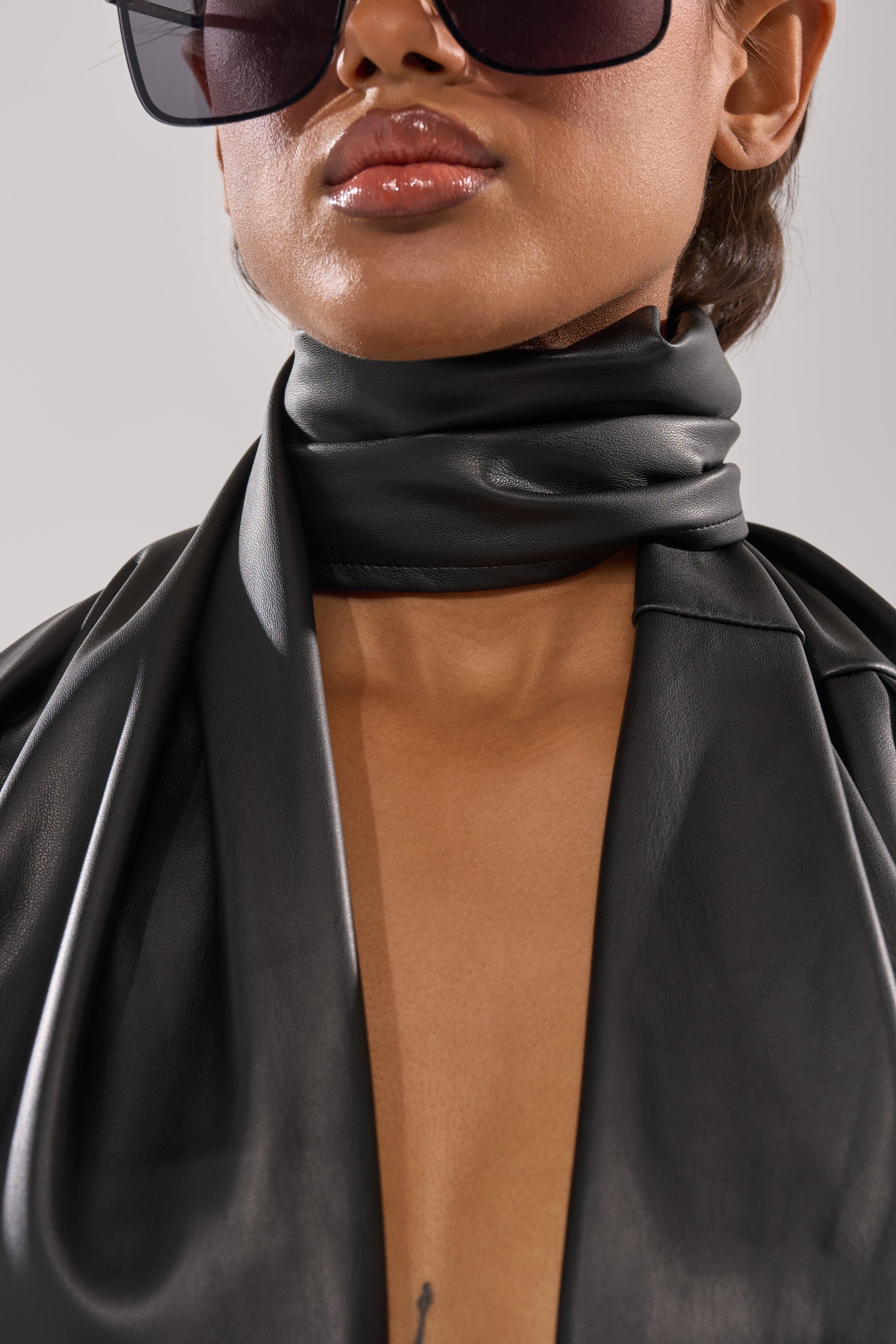 A person wearing large black sunglasses, glossy lipstick, and an AKIRA Label black leather outfit with the VALLY PU SCARF PANT stylishly wrapped around their neck. The image is cropped from the nose down. 5