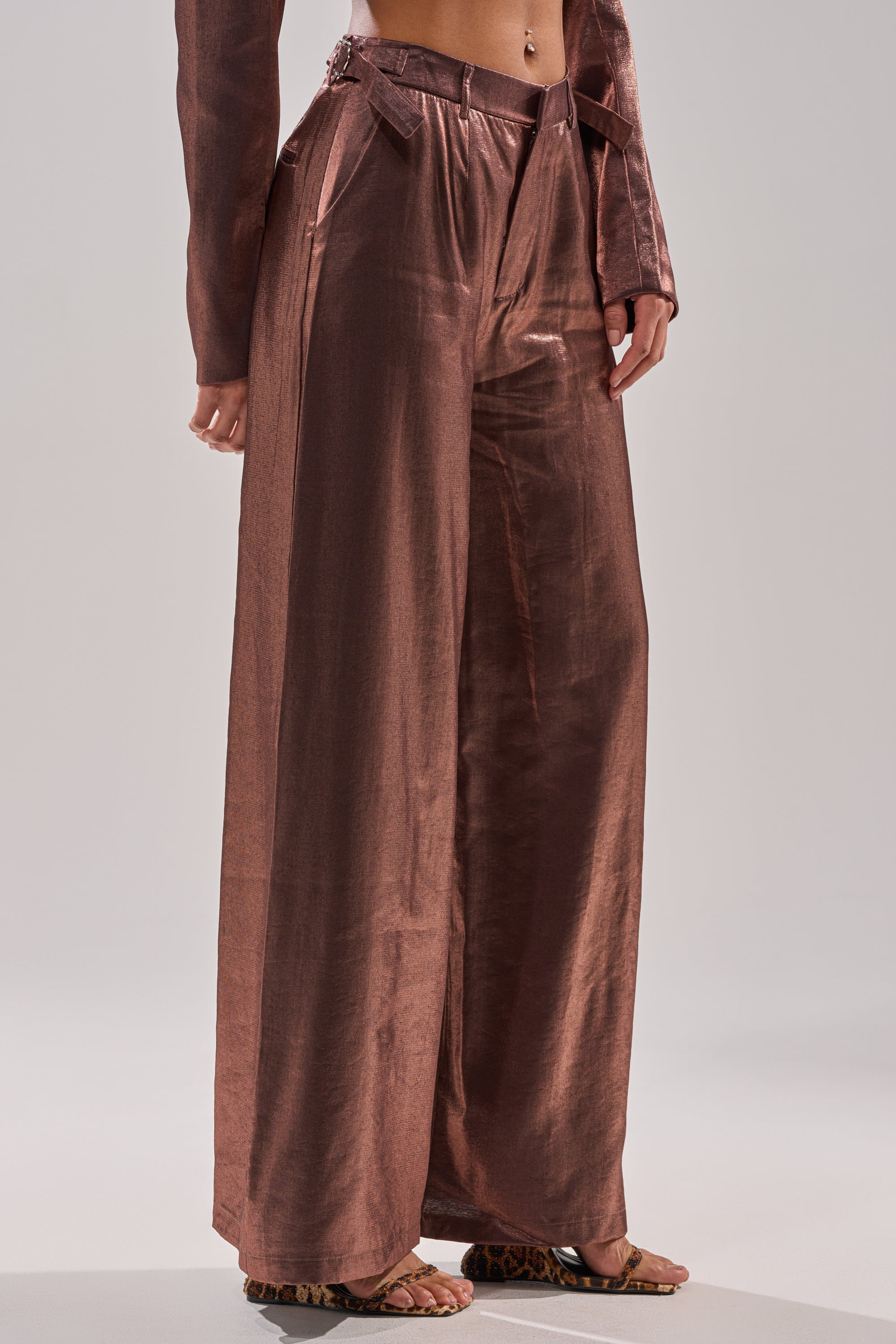 A person wears the STAY CLOSE IRIDESCENT TROUSER featuring a wide-leg silhouette, paired with a chic jacket and animal print sandals. Only the lower half of the body appears against a plain background. 3