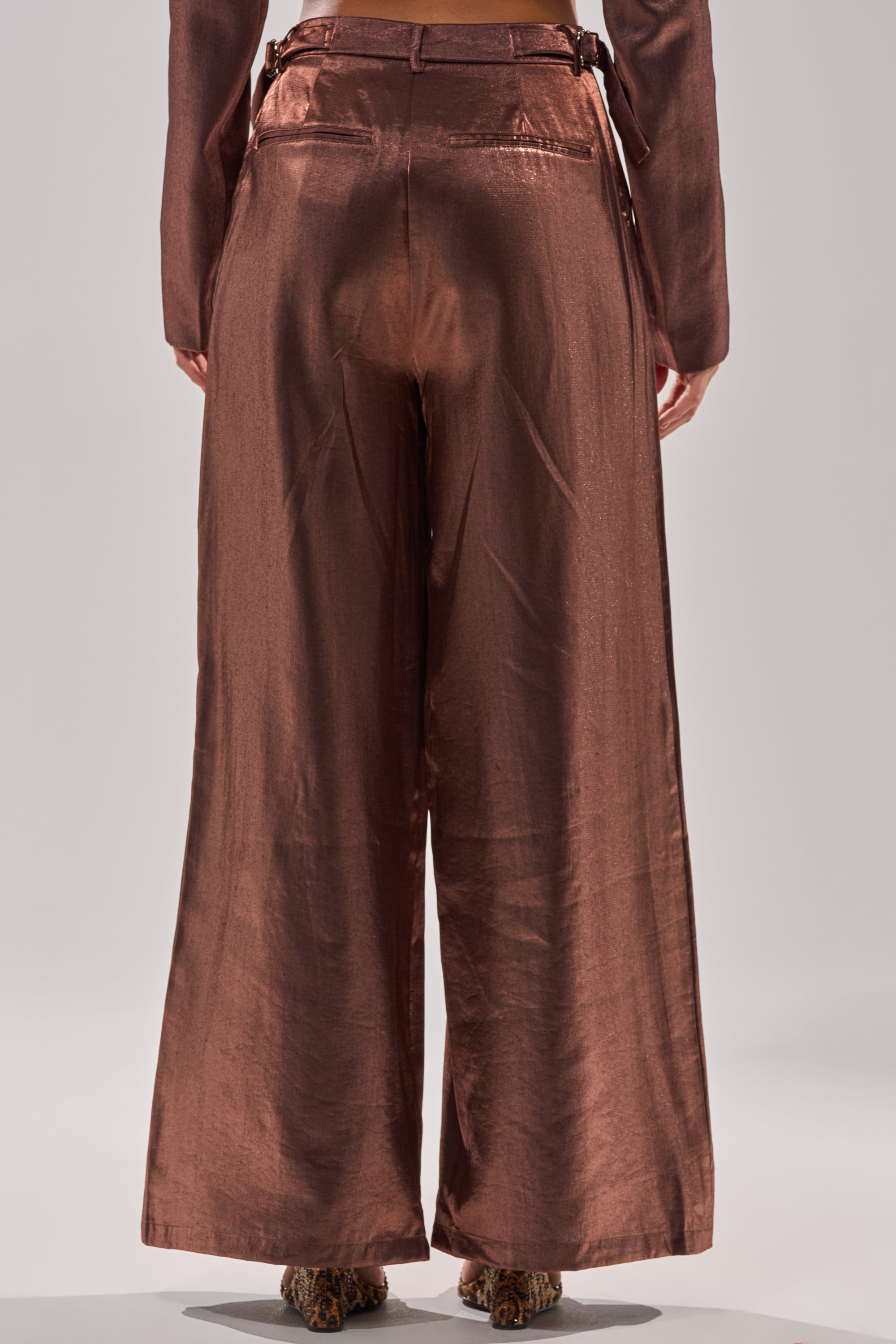 A person is shown from the back wearing STAY CLOSE IRIDESCENT TROUSER, featuring a shiny, metallic wide-leg silhouette, with a matching long-sleeve top against a plain light background. 4