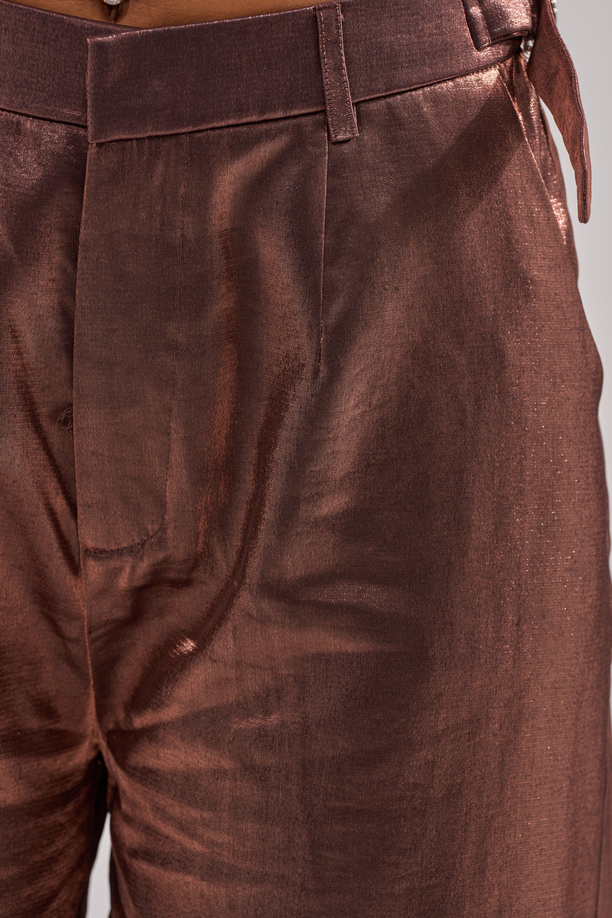 Close-up of a person wearing the STAY CLOSE IRIDESCENT TROUSER, featuring shiny metallic taffeta, belt loops, a structured waistband, detailed seams, and a bold wide-leg silhouette. 7