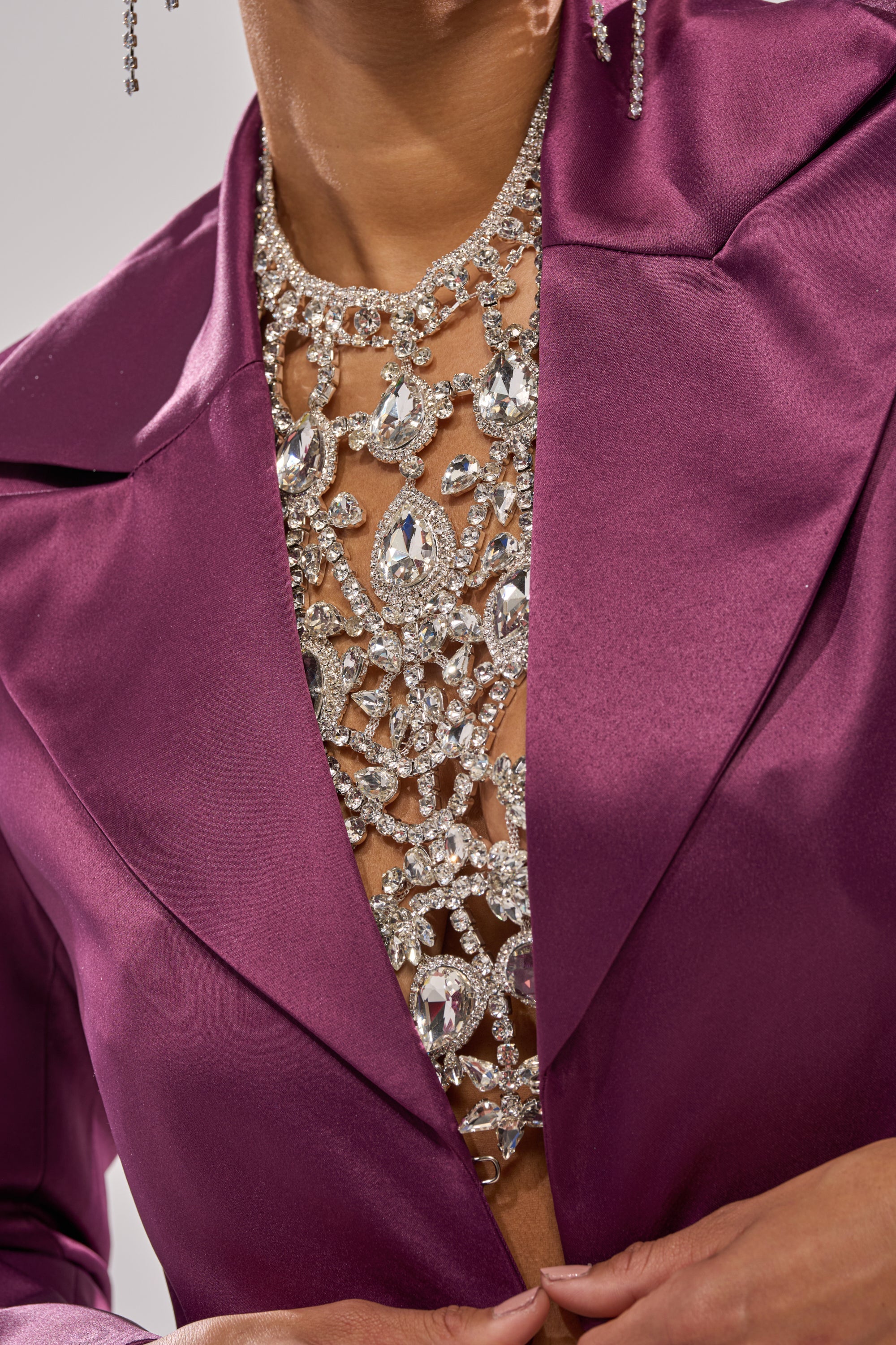 A person wears a shiny magenta blazer over the IN YOUR DREAMS BODY CHAIN, which sparkles and covers their chest for a glamorous look. Only their lower face and torso are visible. 2
