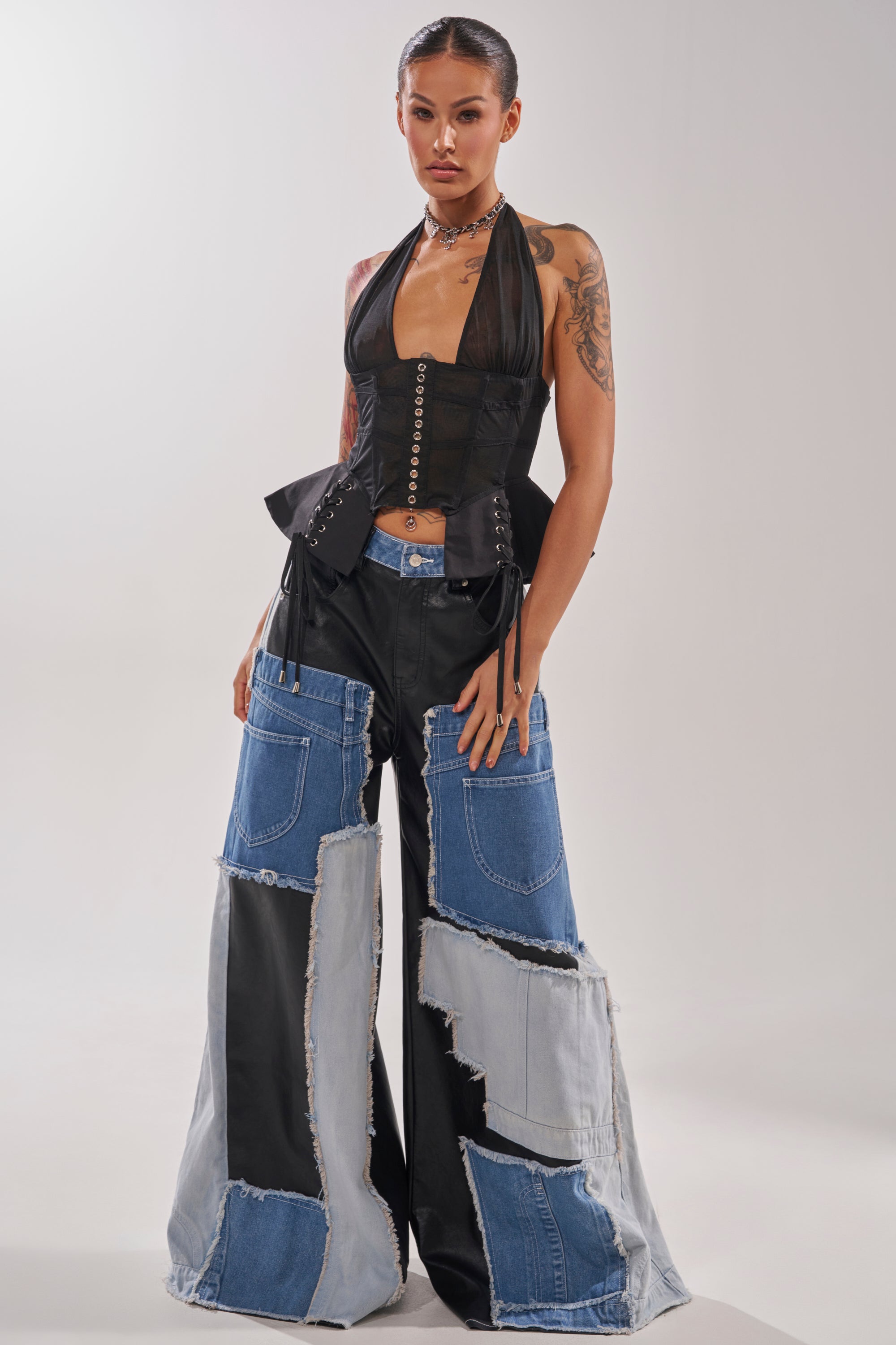 A woman exudes confidence in a black halter corset top and the TOO MUCH GOING ON RELAXED DENIM, showcasing visible seams and frayed edges, embodying street style against a plain light background. 1