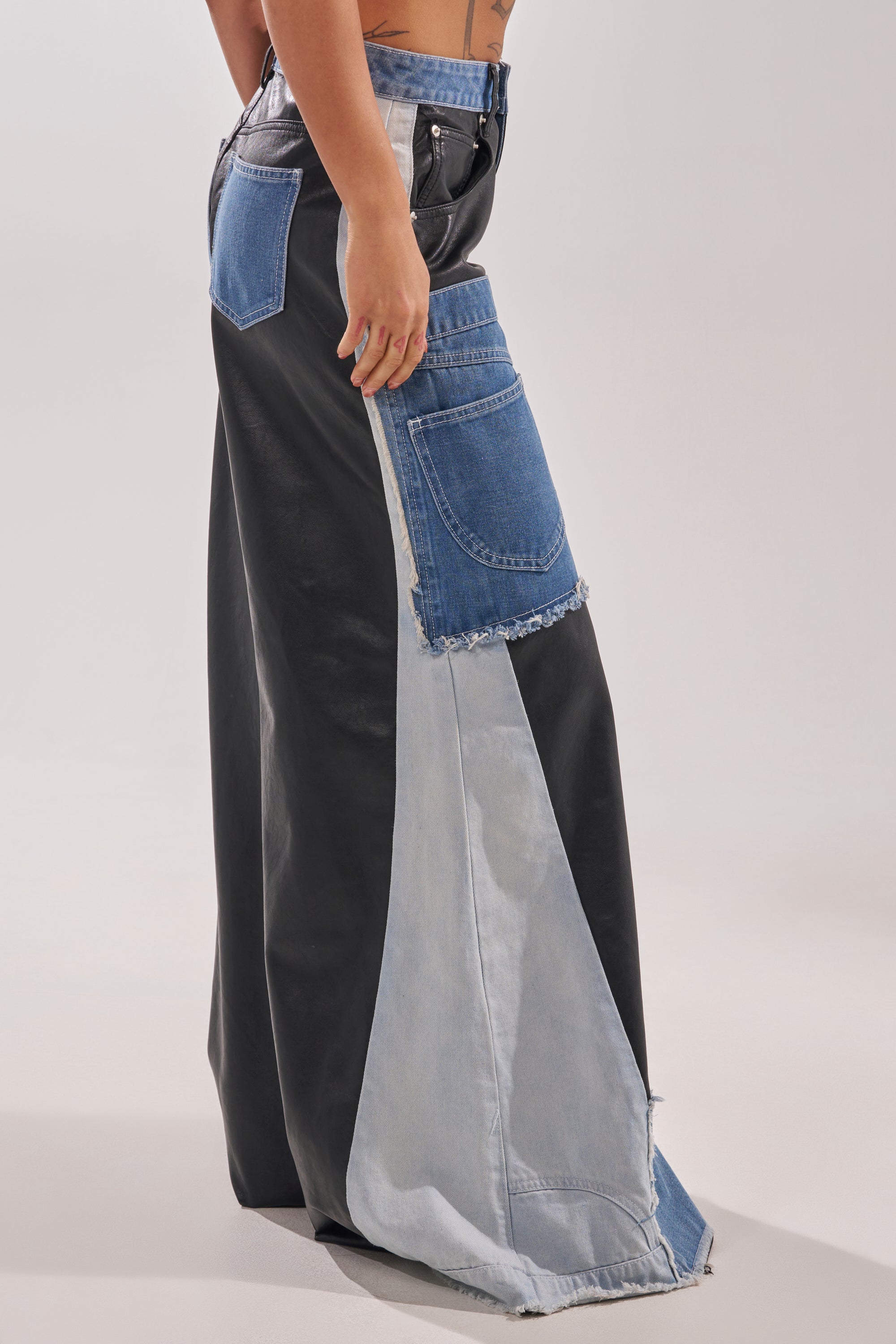 A person showcases street style in the TOO MUCH GOING ON RELAXED DENIM skirt, featuring black faux leather, blue denim patchwork, large jean pockets, and exposed seams. 5