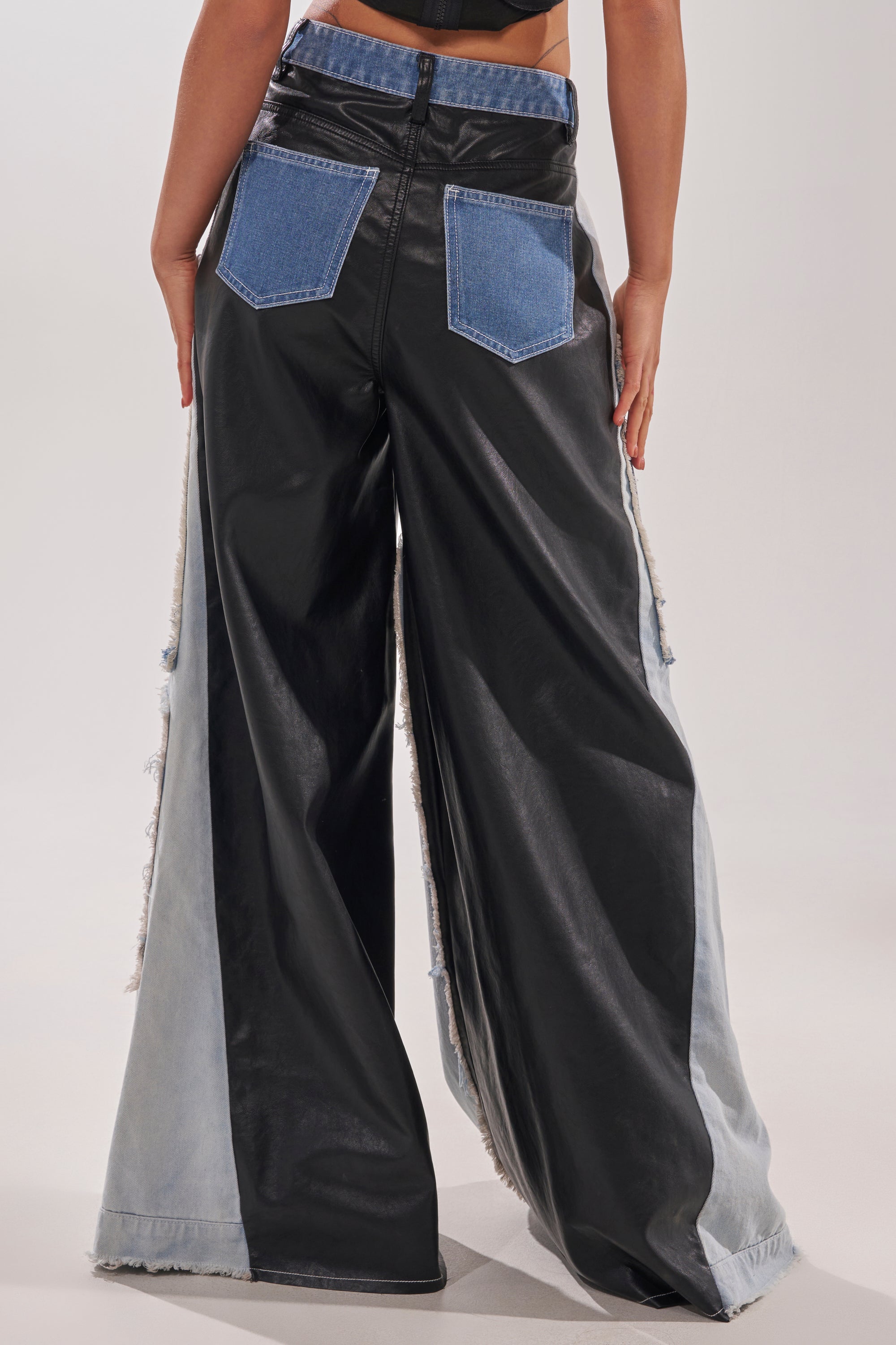 A person wears the TOO MUCH GOING ON RELAXED DENIM: street style wide-leg pants featuring black faux leather on the back and inner panels, light denim sides, and blue denim back pockets. Shown waist down, from behind. 6