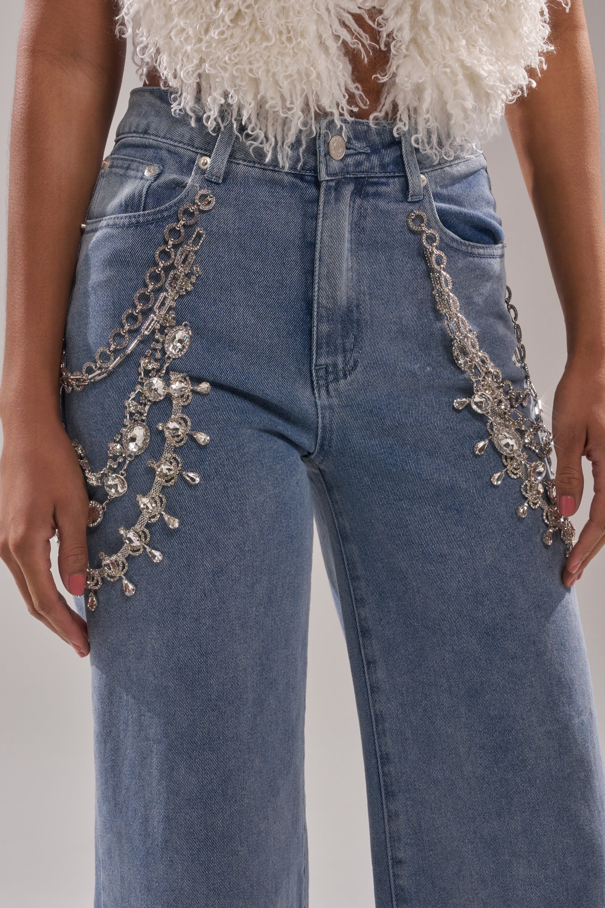 Someone wearing DIAMOND LOVER RELAXED DENIM WITH RHINESTONE—wide-leg jeans featuring rhinestone and chain embellishments at the hips and thighs—paired with a white, textured sleeveless top. 8