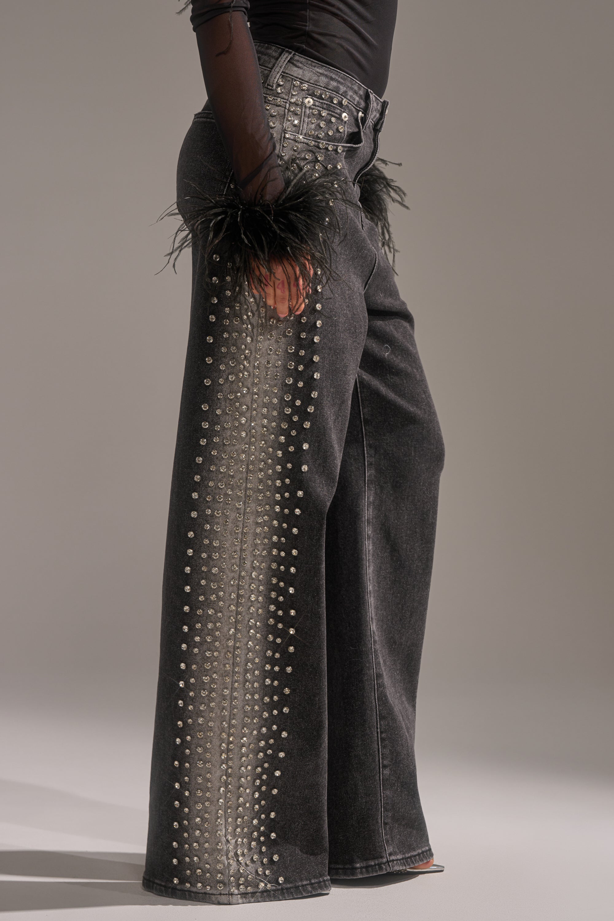 Wearing the FREAKING FIRE EMBELLISHED DENIM, wide-leg black jeans decked with rows of silver rhinestones, styled with a black top featuring feathery cuffs.
