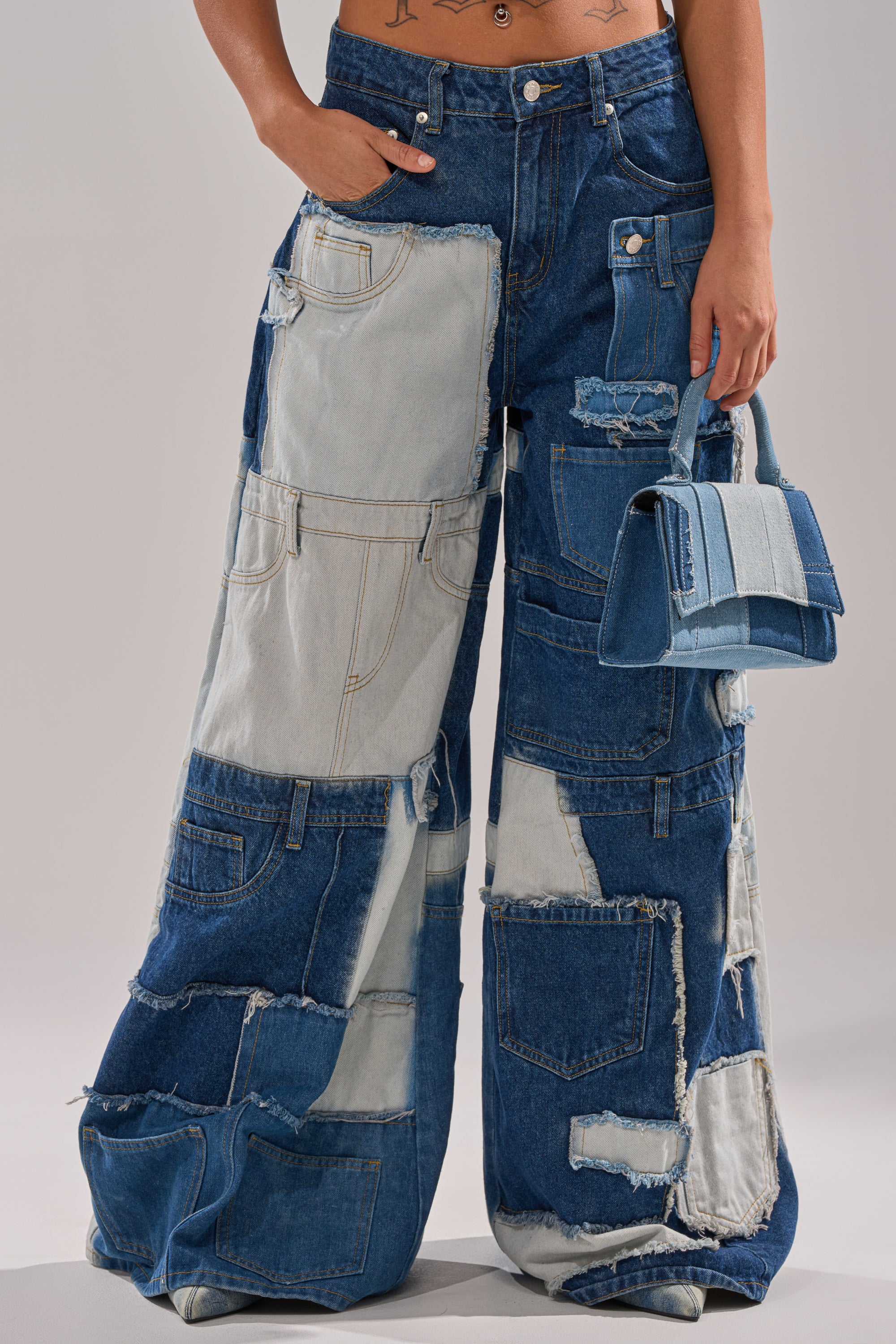 A model showcases the TOO MUCH GOING ON WIDE LEG DENIM, high-waisted patchwork jeans with a matching small denim handbag. The image displays only the lower torso and legs against a plain background. 2