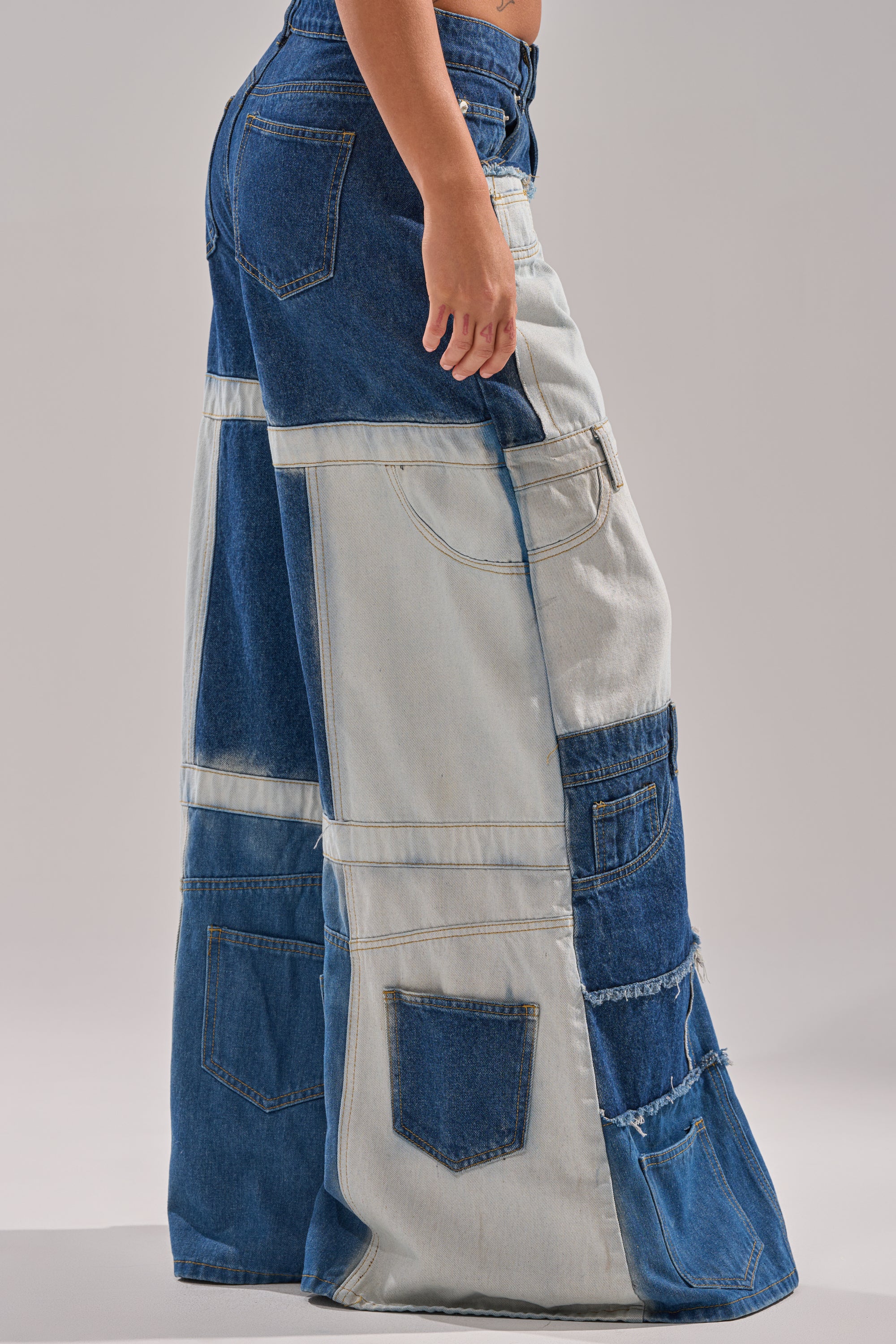 Wearing the TOO MUCH GOING ON WIDE LEG DENIM, featuring high-waisted patchwork in light and dark blue with wide legs, multiple pockets, and visible seams, a person stands against a plain light background. 3