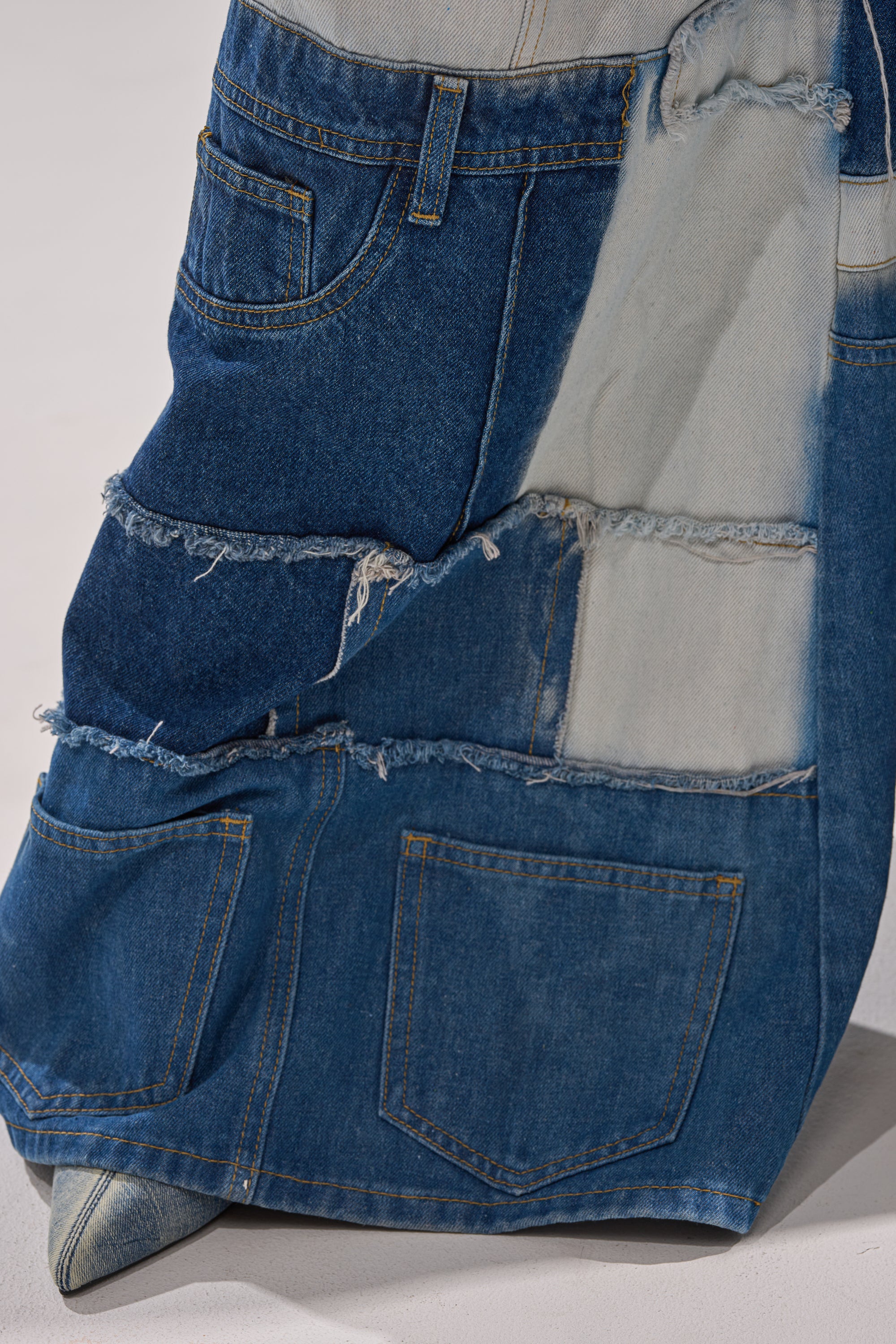 A close-up of the TOO MUCH GOING ON WIDE LEG DENIM, showcasing patchwork in varied blue shades with visible seams, frayed edges, and design elements inspired by high-waisted and patchwork jeans styles. 8