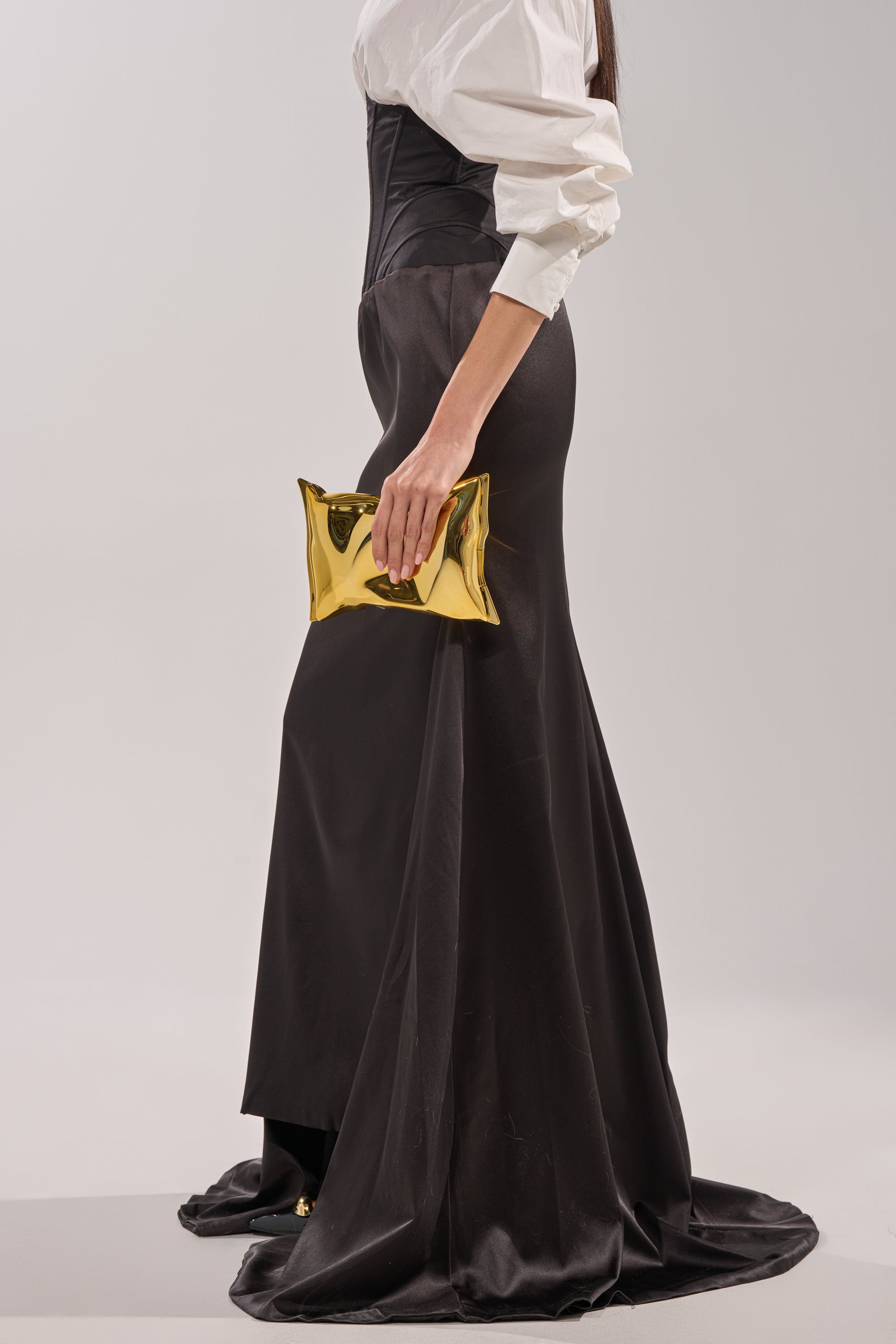 Wearing the STAR OF THE NIGHT HIGH WAISTED CORSET MAXI SKIRT with a white blouse and black corset, a person holds a shiny gold clutch. Only their lower body and one arm are visible against a plain light background. 2