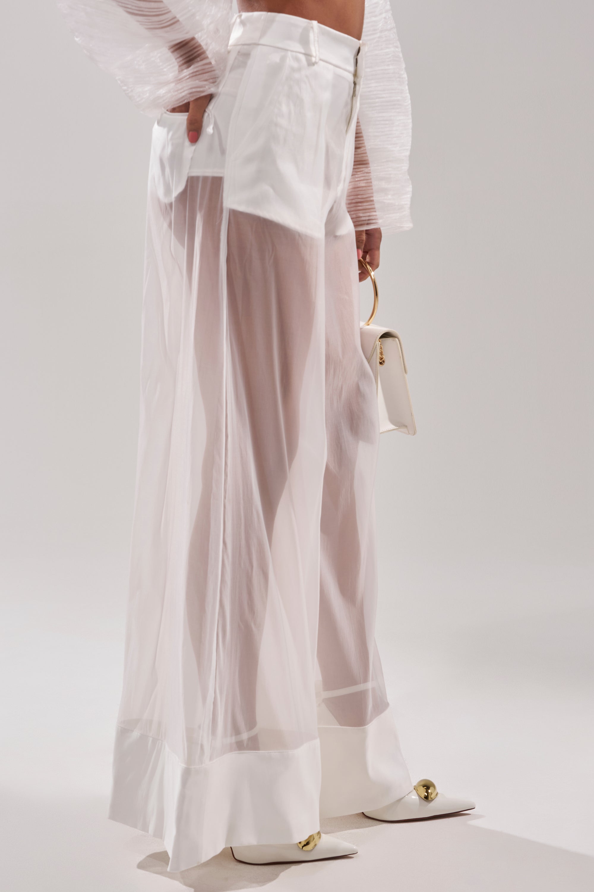 Wearing the VACATION MODE TROUSER—sheer organza pants over white shorts—with pointed-toe heels and a chic white handbag, this modern outfit features stylish wide-leg trousers perfect for any occasion. 3
