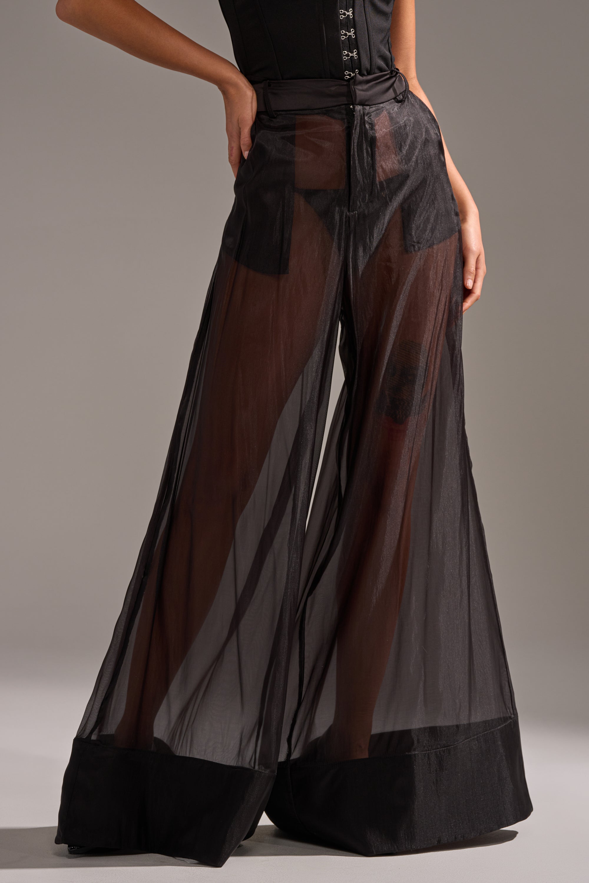 A person wears the LOUD AND LUX TROUSER—sheer, lightweight wide-leg pants with a solid black waistband and cuffs—over black shorts, paired with a black top. The high-rise style stands out against a neutral gray background. 1