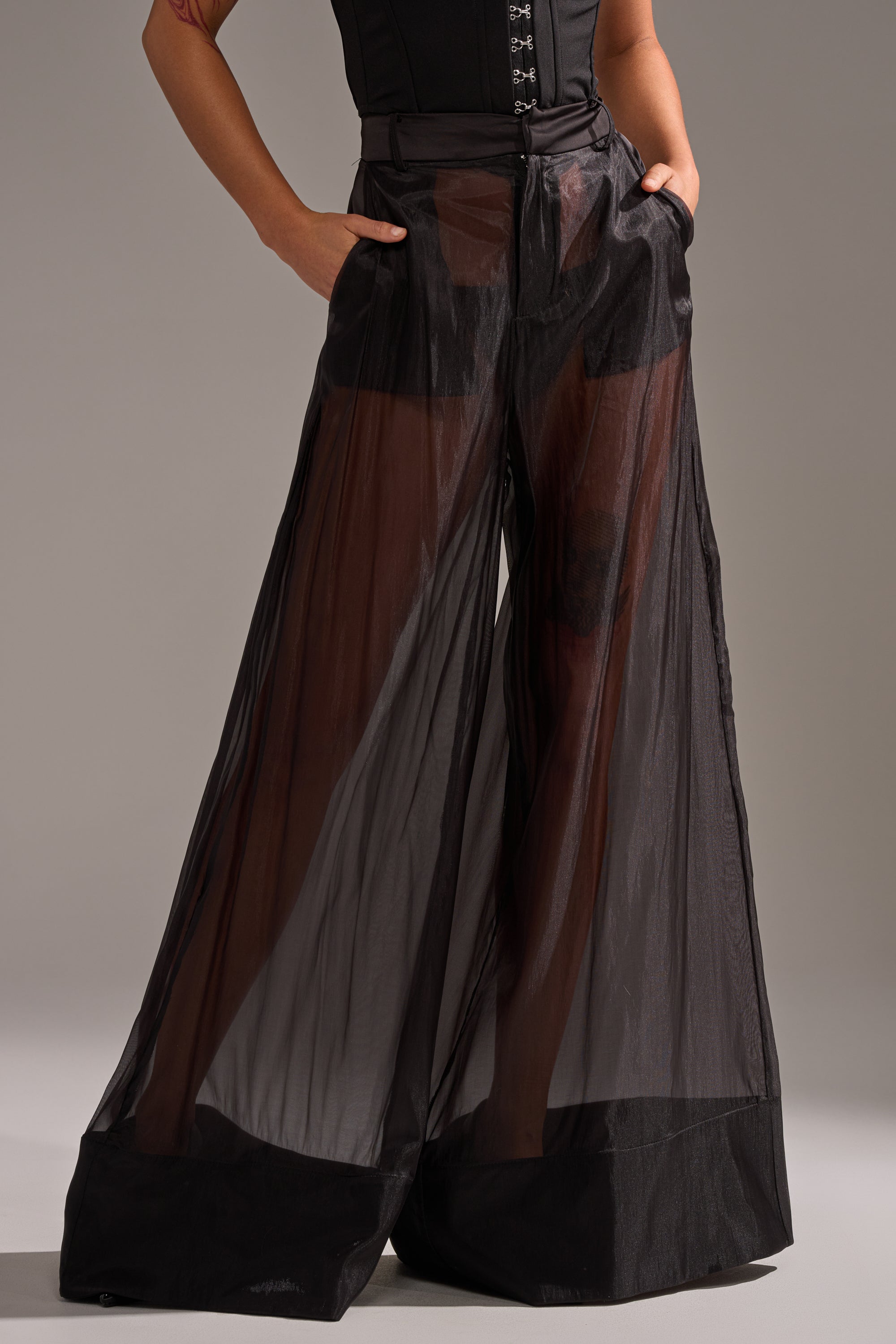 A person wears the LOUD AND LUX TROUSER—high-rise, sheer black wide-leg pants with pockets; the transparent fabric reveals black undergarments. Upper body and face are not shown. 2