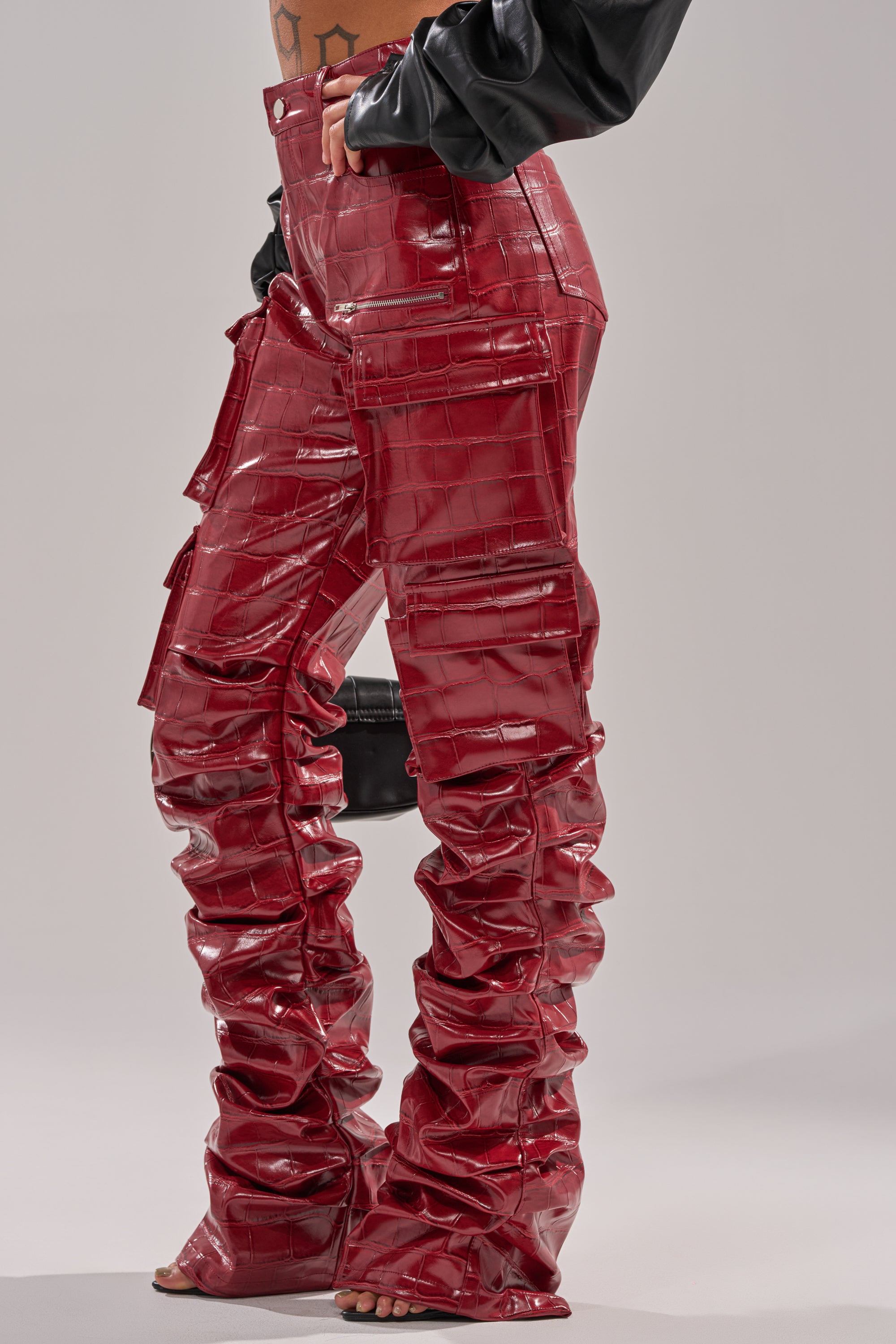 Wearing the STRAIGHT TO THE POINT STACKED FAUX LEATHER TROUSER—shiny, crocodile-embossed with multiple pockets and a ruched, stacked leg—a person stands on tiptoe, showing a glimpse of their torso.