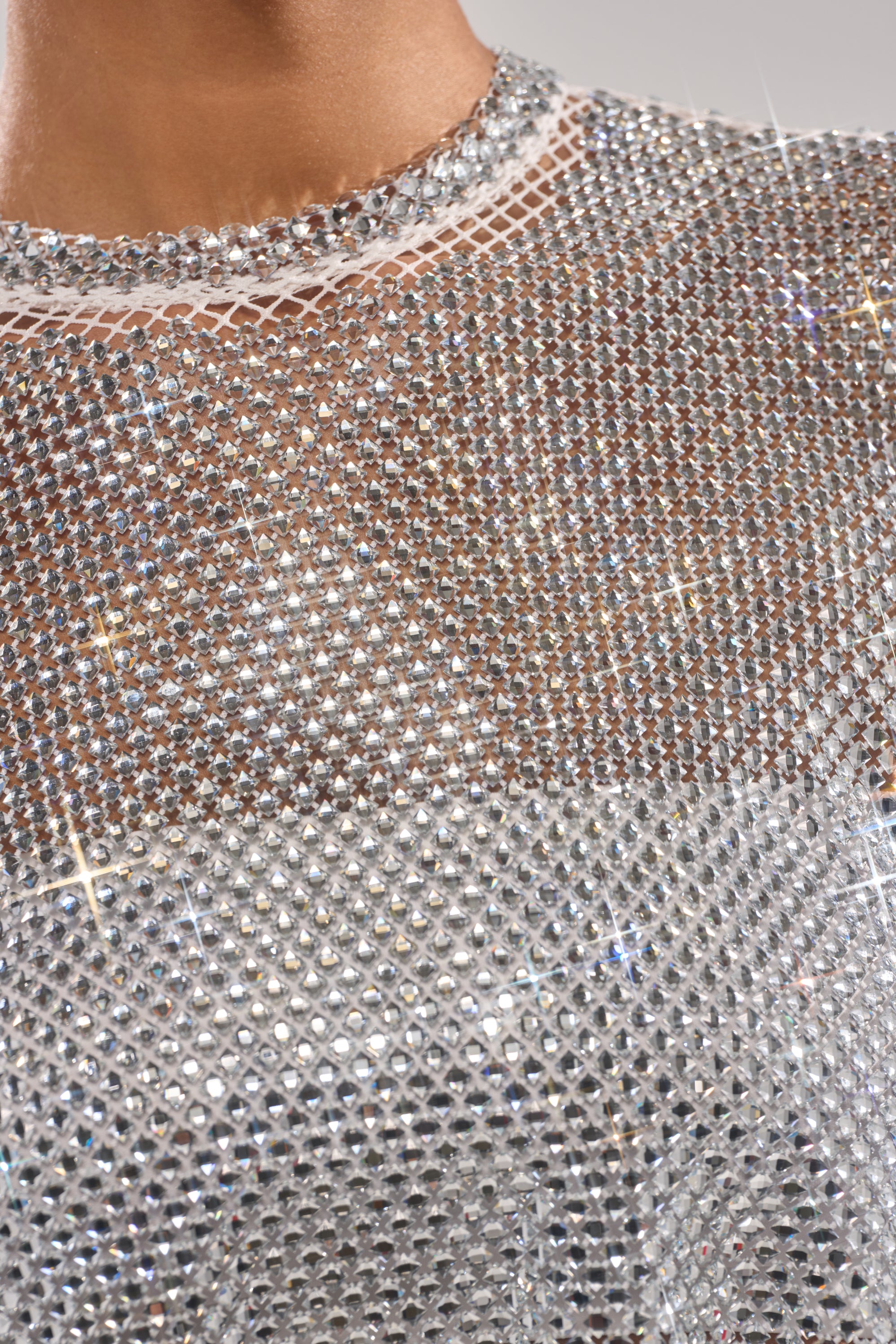 Close-up of a person's upper chest and neckline wearing the JUST A FEELING RHINESTONE TEE—this sparkling, silver, rhinestone-studded cropped top catches the light for a glittering, luxurious look.