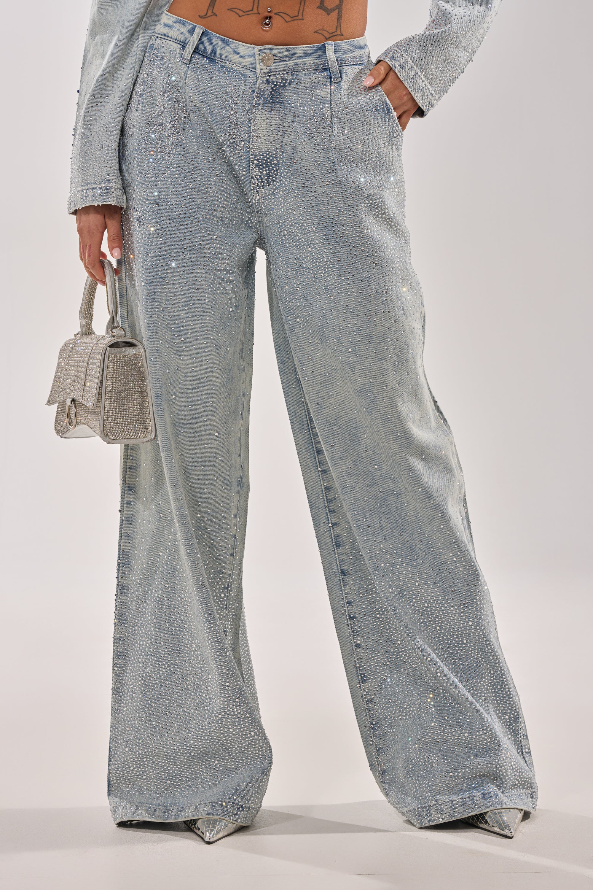A person wears the LIGHTS OUT RHINESTONE WIDE LEG DENIM with a matching jacket, styled trendily with a small silver handbag; only the lower torso and legs are visible. 2