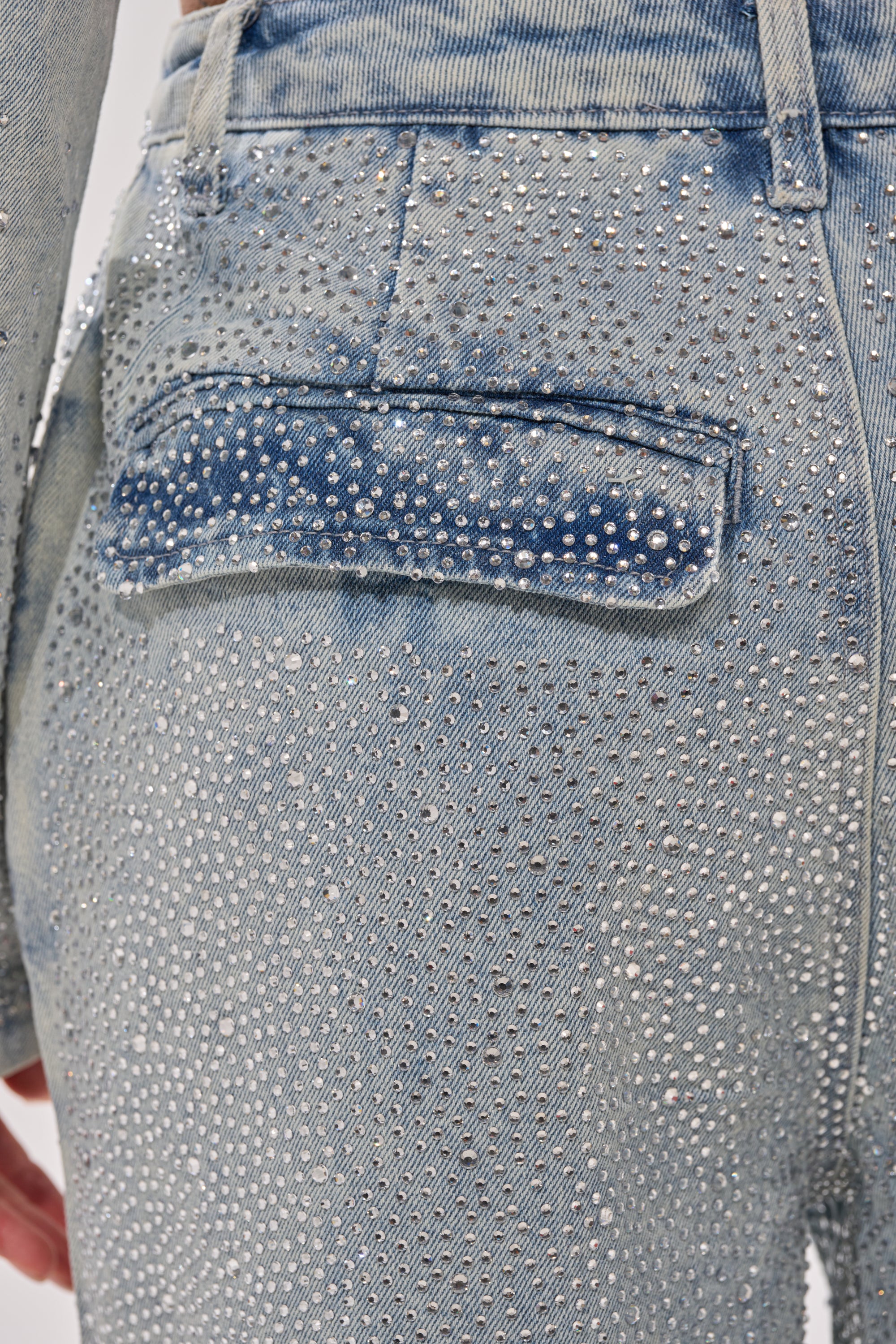Close-up of the back pocket area of LIGHTS OUT RHINESTONE WIDE LEG DENIM, showcasing sparkling light blue high-rise denim adorned with numerous small, shiny rhinestones. 7