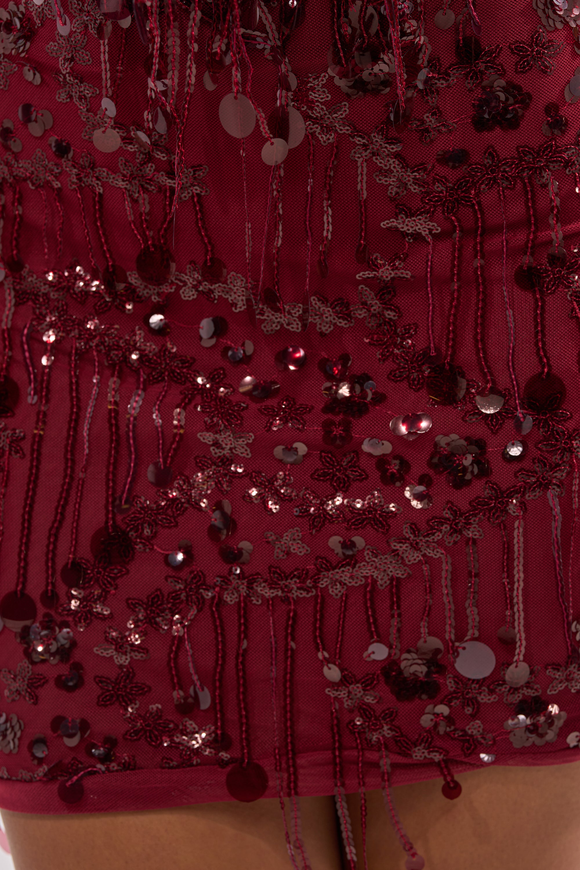 Close-up of the MOOD FOR THE NIGHT SEQUIN MINI DRESS in wine red, featuring off-the-shoulder style with intricate floral sequin and bead embellishments. Dangling strands catch the light, highlighting its sparkling details.