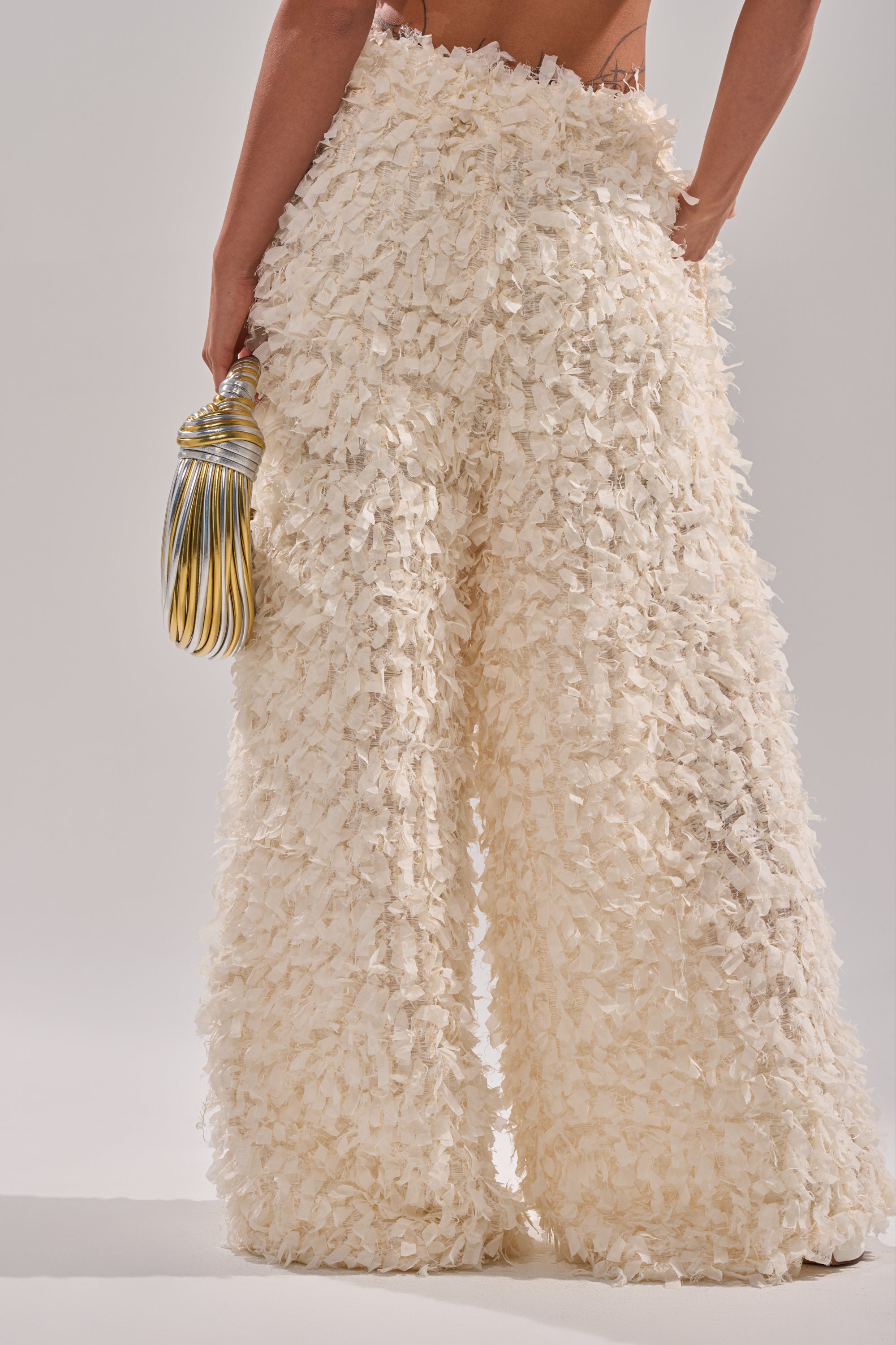 A person wearing the MOXIE WIDE LEG TROUSER, featuring high-rise wide legs and layered petal-like mesh, holds a yellow and silver striped handbag against a plain light background. 3