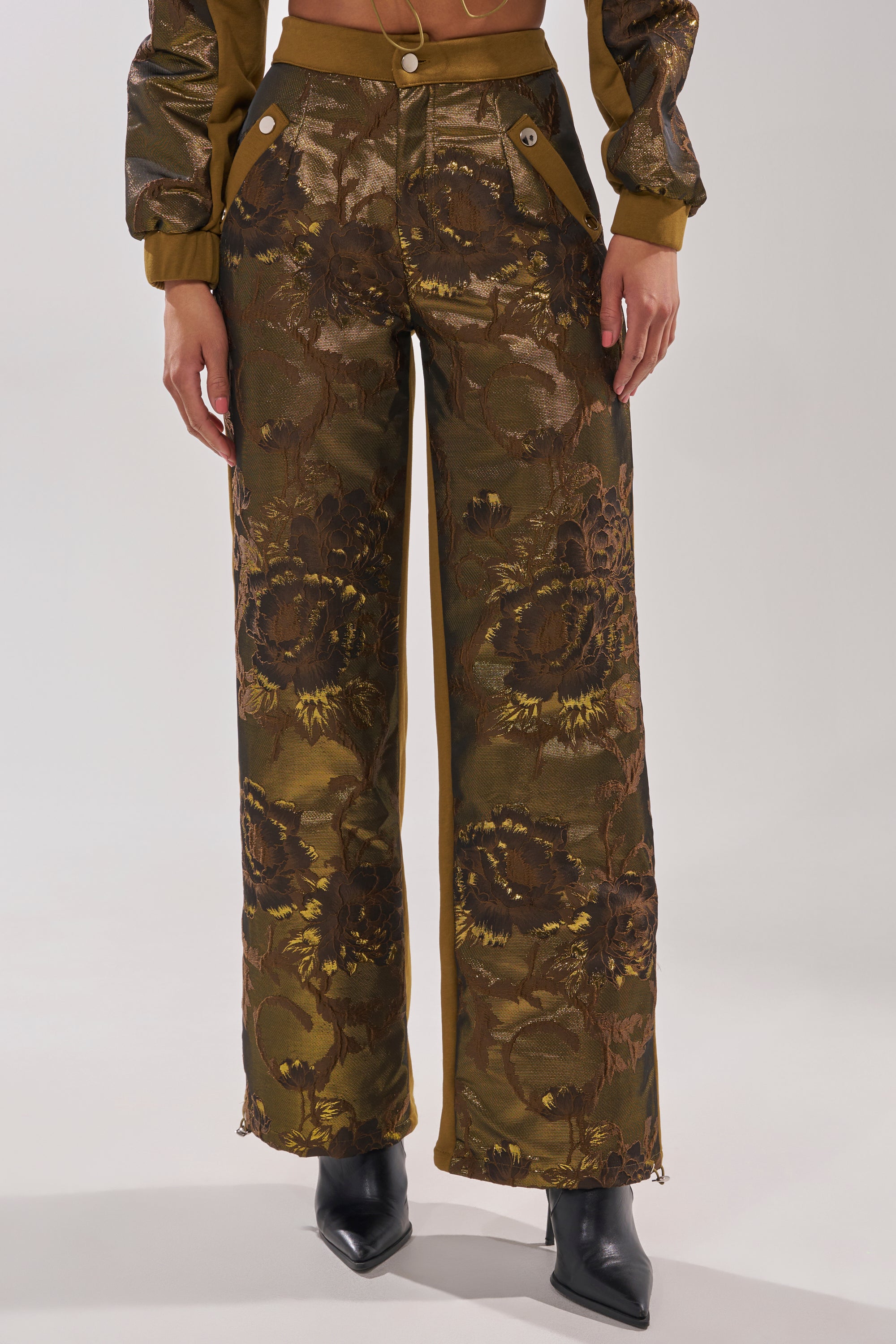 A person wears the YOU KNOW IT BABY WIDE LEG JOGGER, featuring a high-waisted, wide-leg design and metallic brocade finish, paired with a matching jacket and black pointed-toe boots against a light background. 3